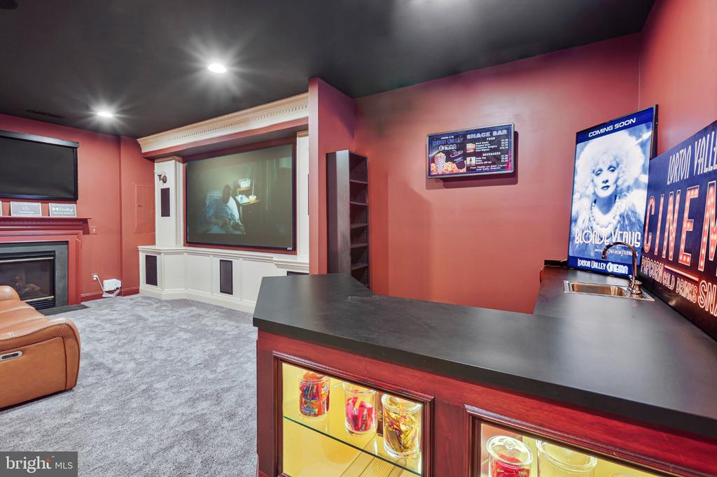 Home theater with a large projection screen, fireplace, and illuminated bar cabinets.