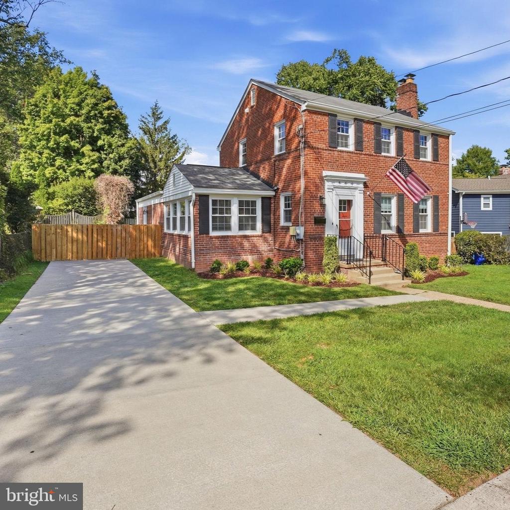 Two-story red-brick house with an American flag, enclosed side addition, and wide concrete driveway.