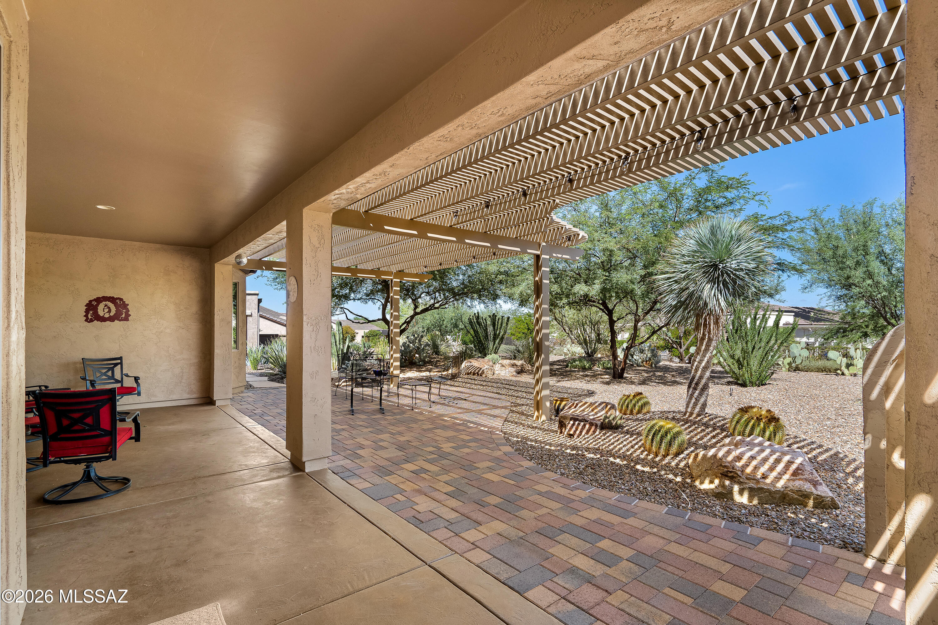 Covered patio with a slatted pergola, paver walkway, and desert landscaping.