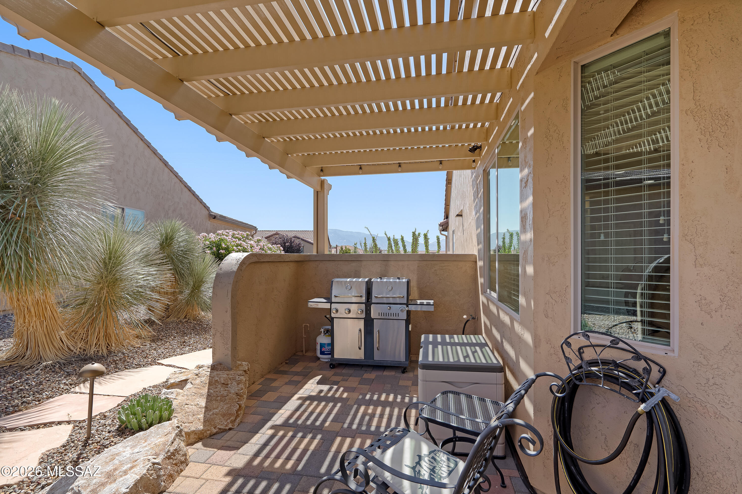 Furnished stucco patio with a pergola, stainless steel grill, desert landscaping, and distant mountain views.