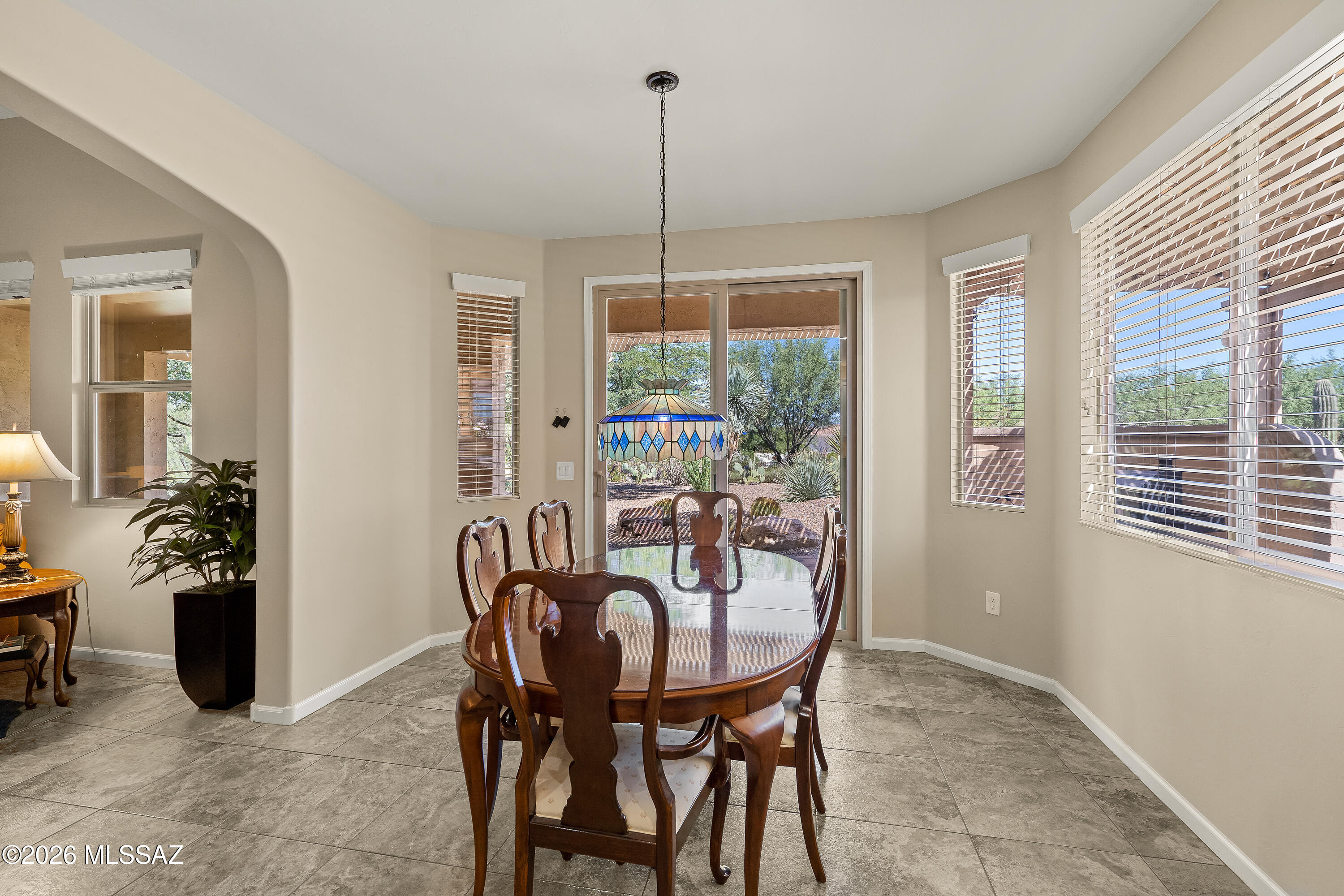 Dining room with a wood table, stained-glass pendant, and sliding doors overlooking desert landscaping.
