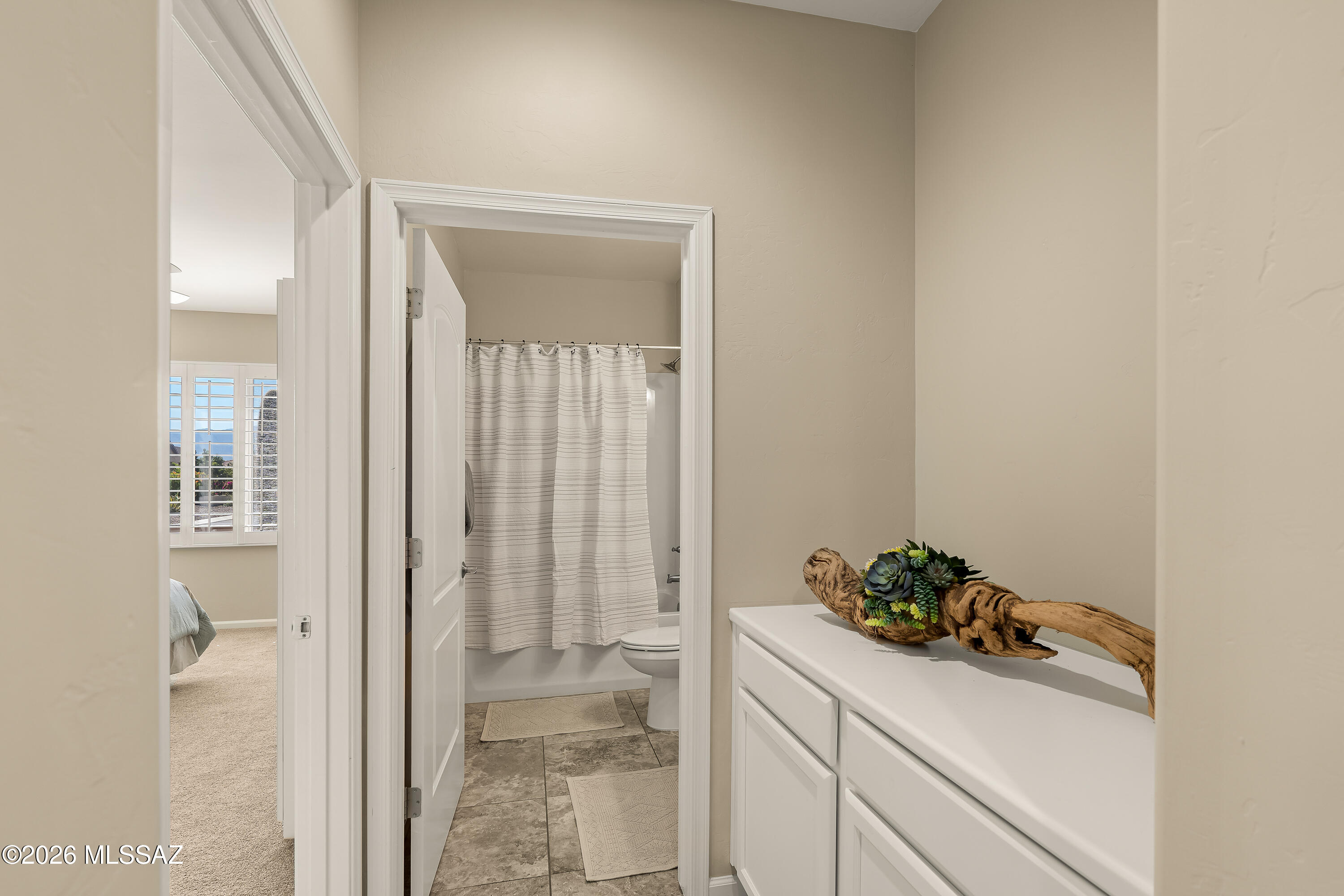 Bathroom vanity with driftwood planter beside a tiled bathroom and striped shower curtain.