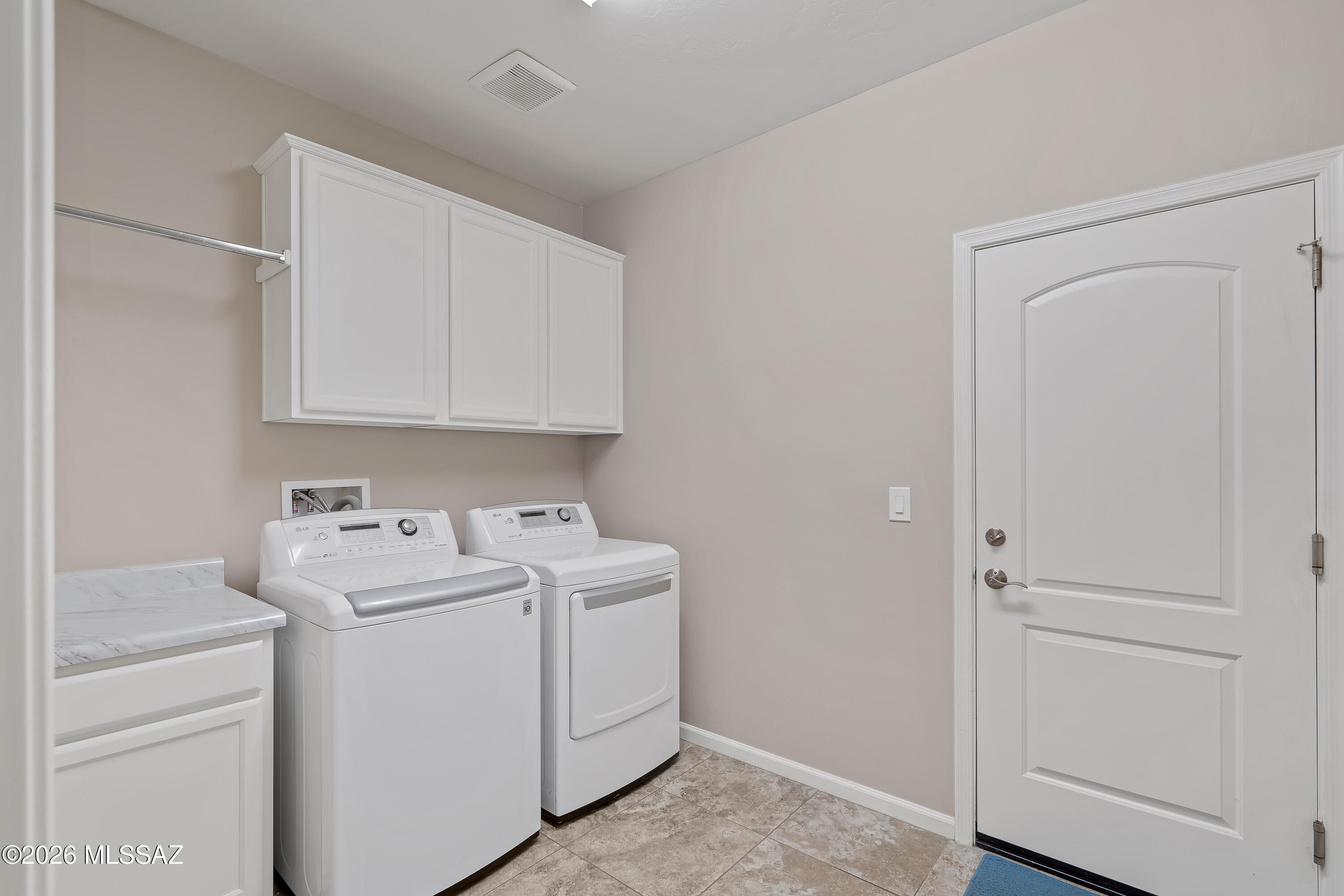 Laundry room with white washer and dryer, overhead cabinets, and a marble-look countertop.