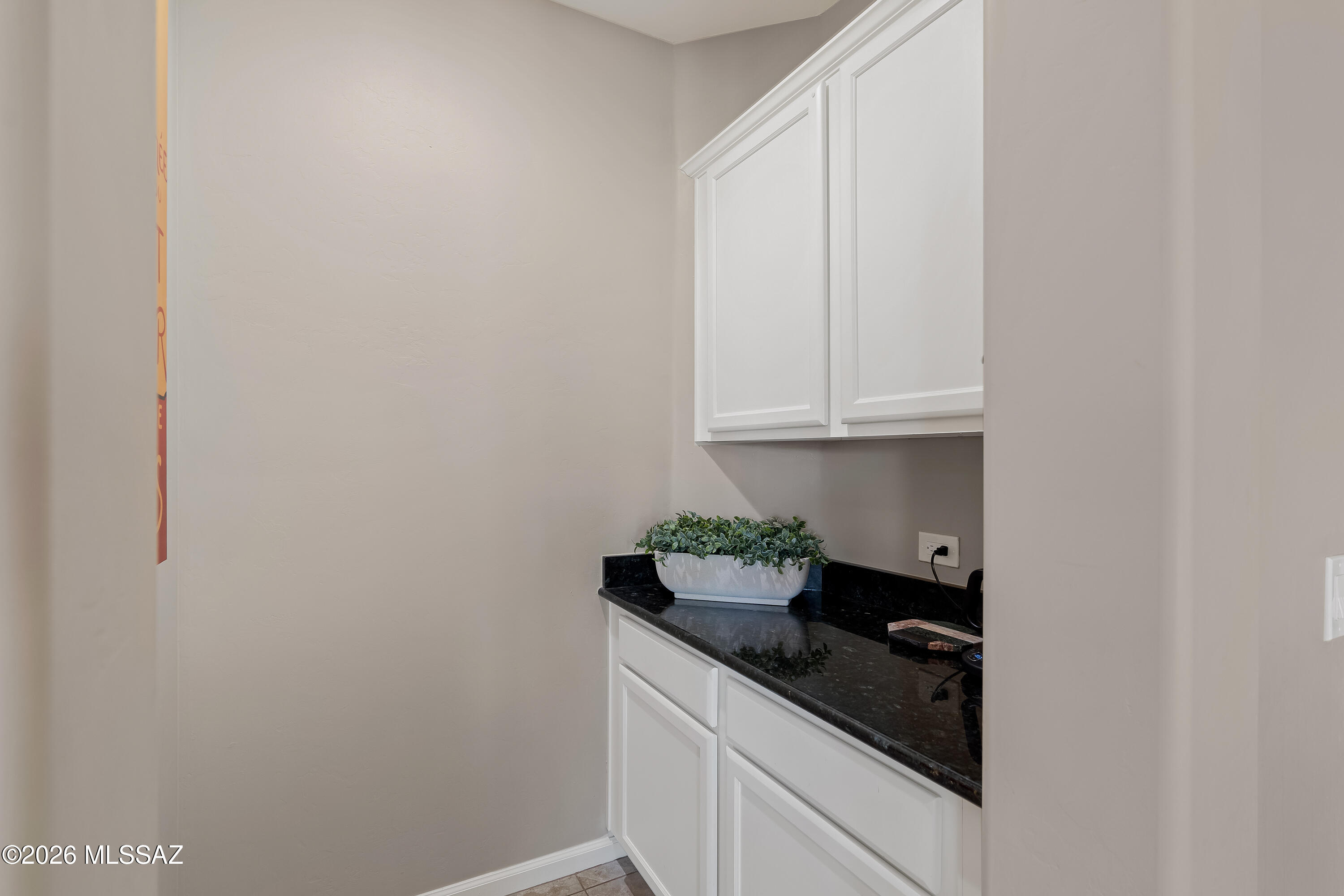 Cabinet-and-counter alcove with white cabinetry, a black countertop, and a planter.