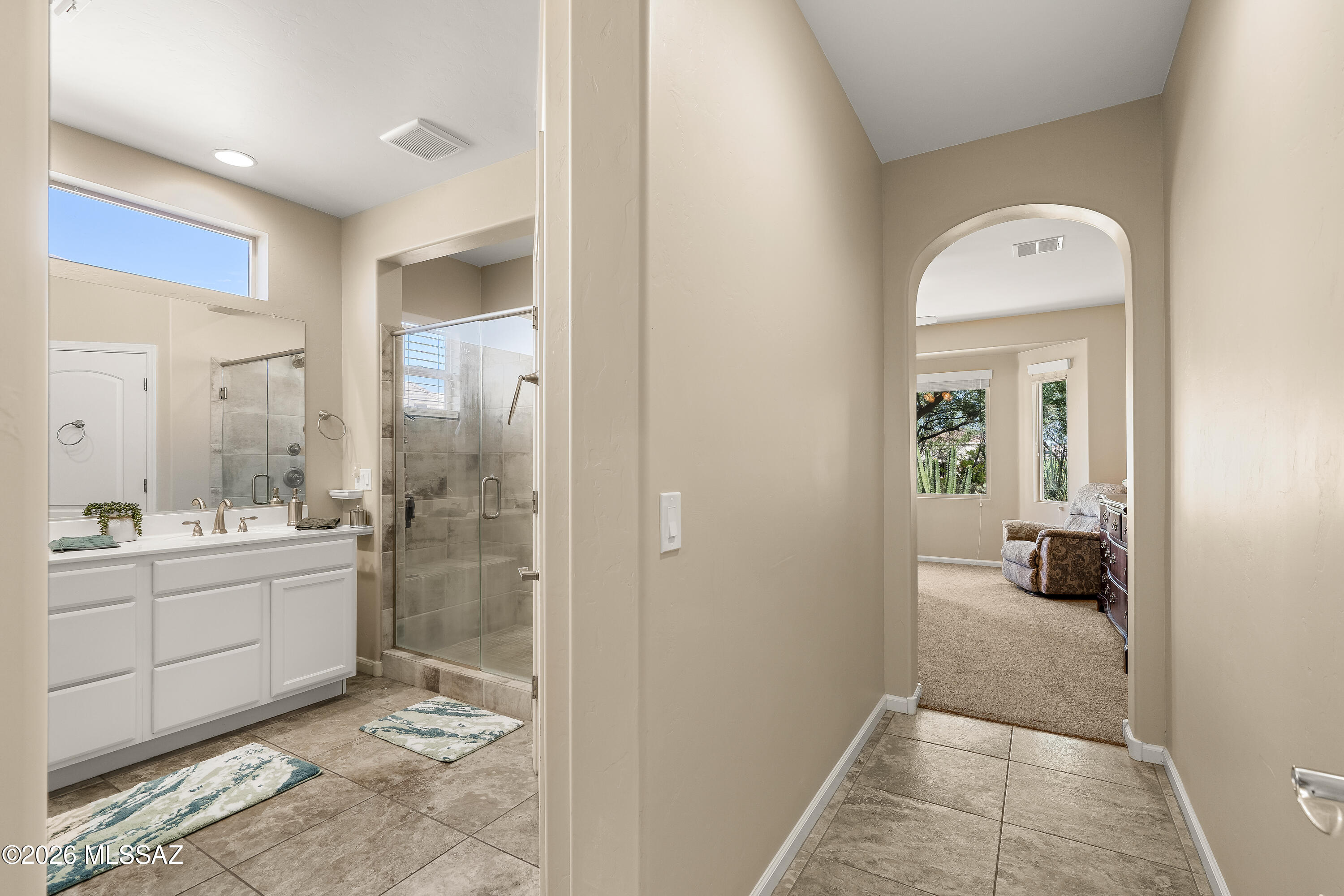 Bathroom with a white vanity and glass shower, opening through an arch to a sitting room.