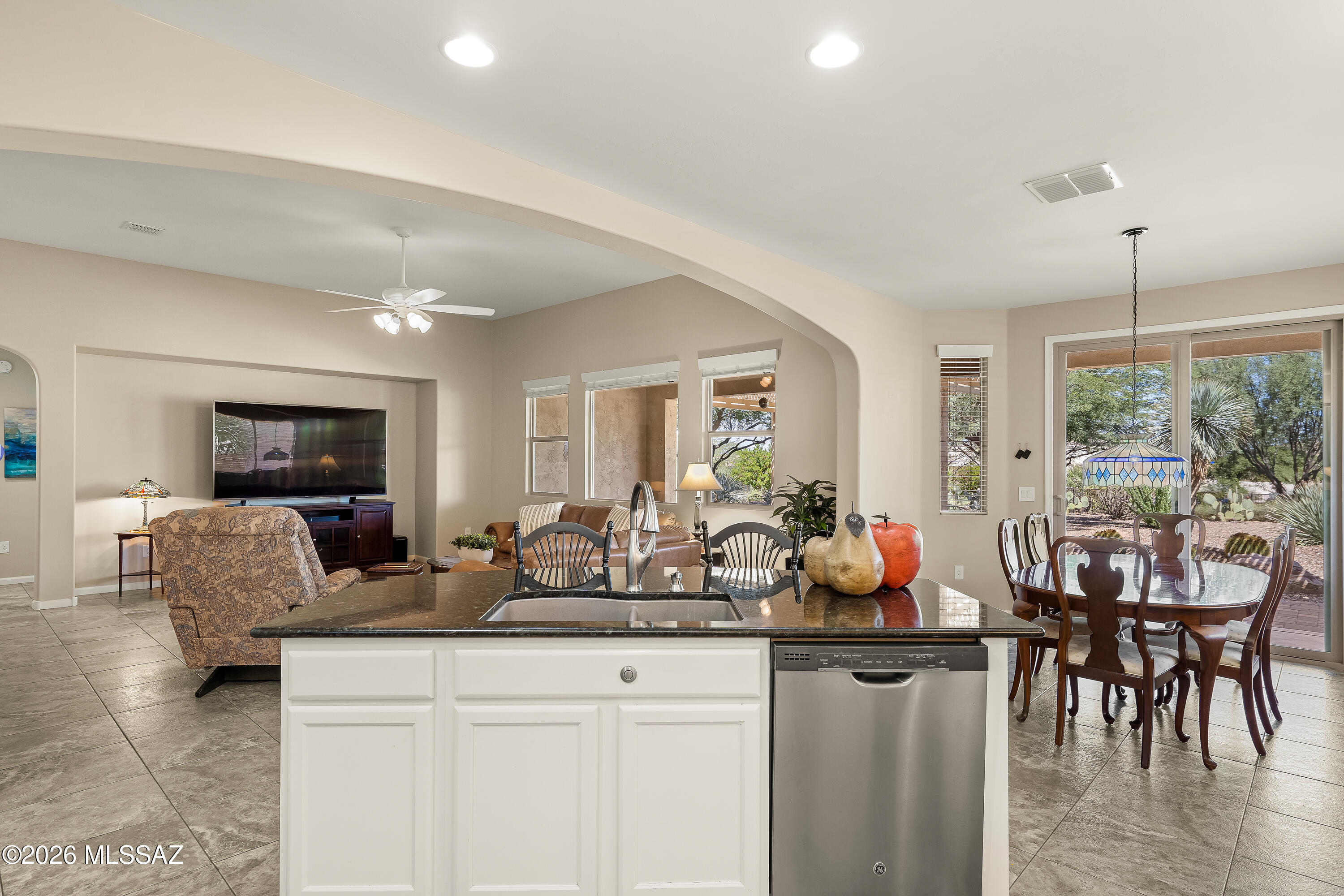 Open-plan kitchen and living area with a stone island, dining table, and sliding doors to a desert garden.