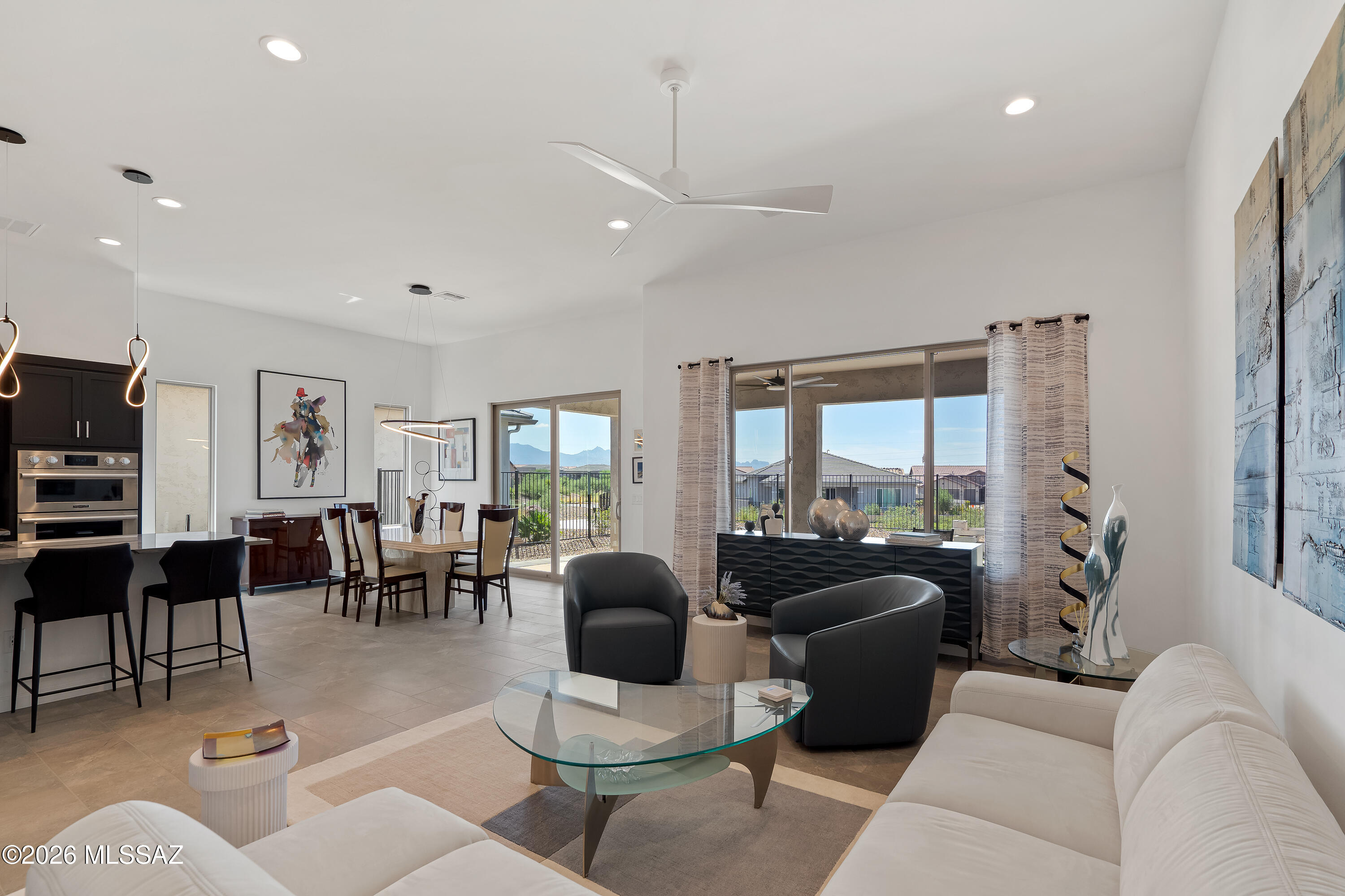 Open-plan living room with white sofas, black chairs, and sliding doors framing a distant mountain view.