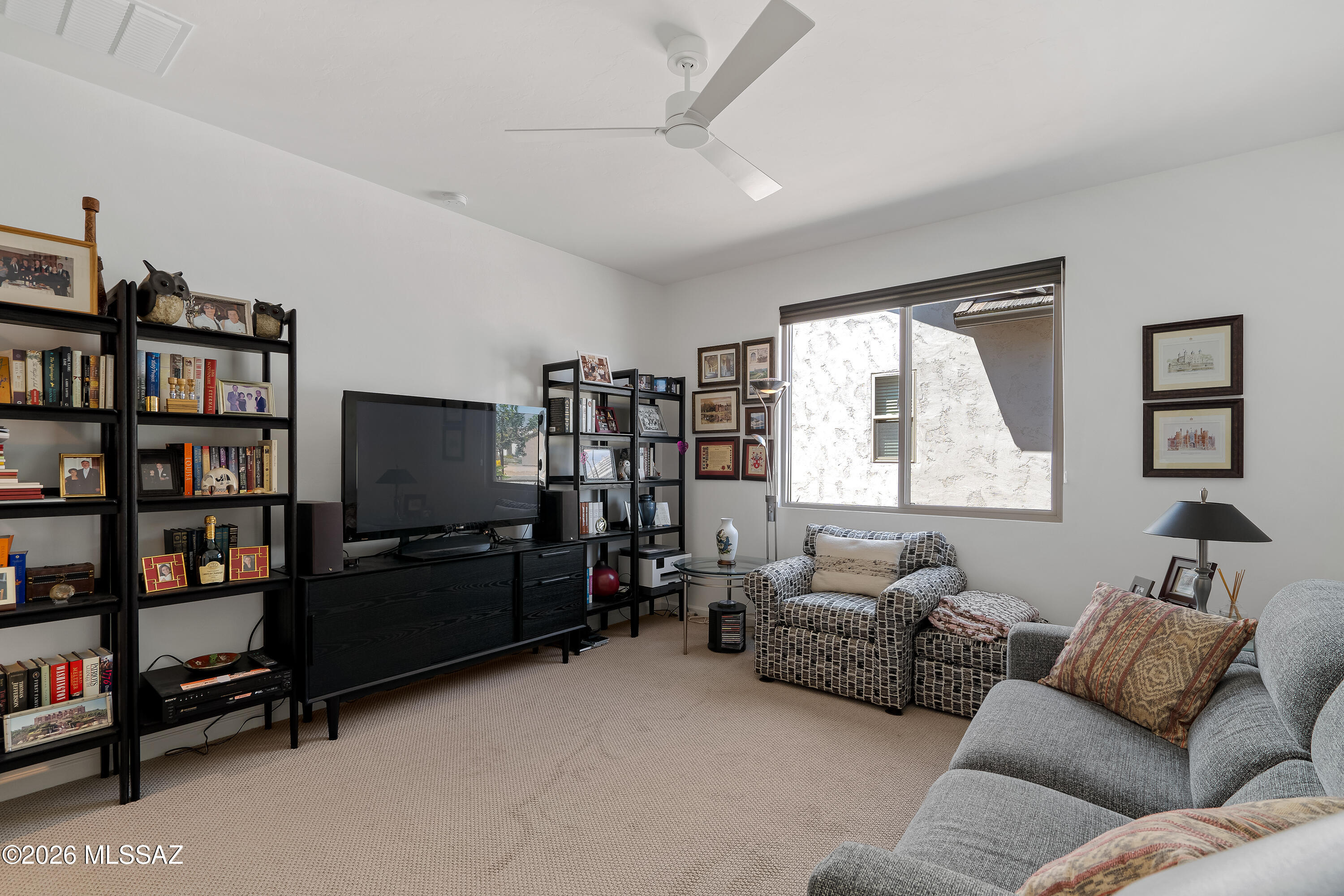 Living room with a gray sofa, patterned armchairs, black bookshelves, and a large window.