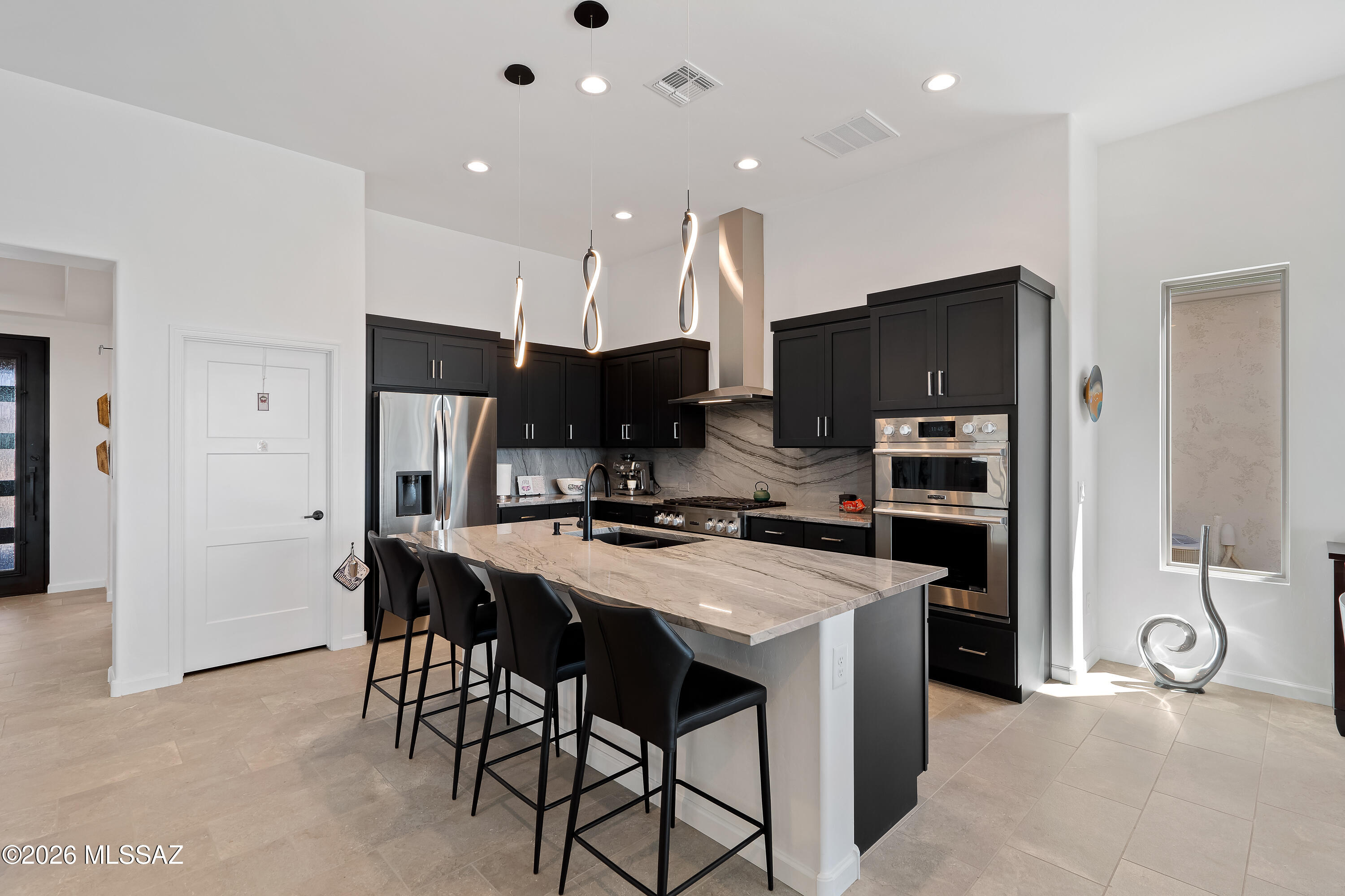 Modern kitchen with black cabinets, stainless steel appliances, and a large veined stone island with bar stools.