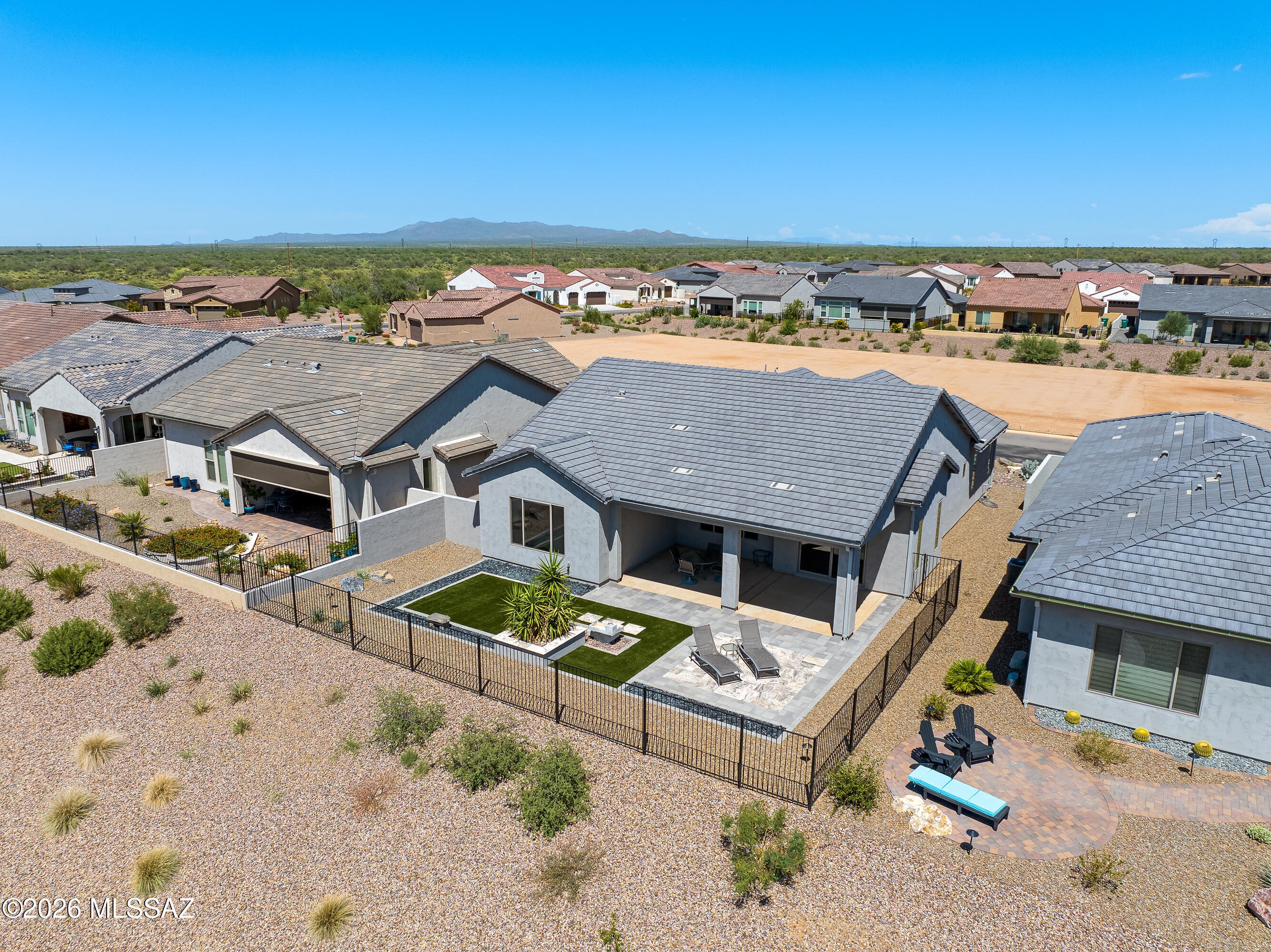 Aerial view of a desert home with a fenced turf yard, covered patio, and mountain backdrop.