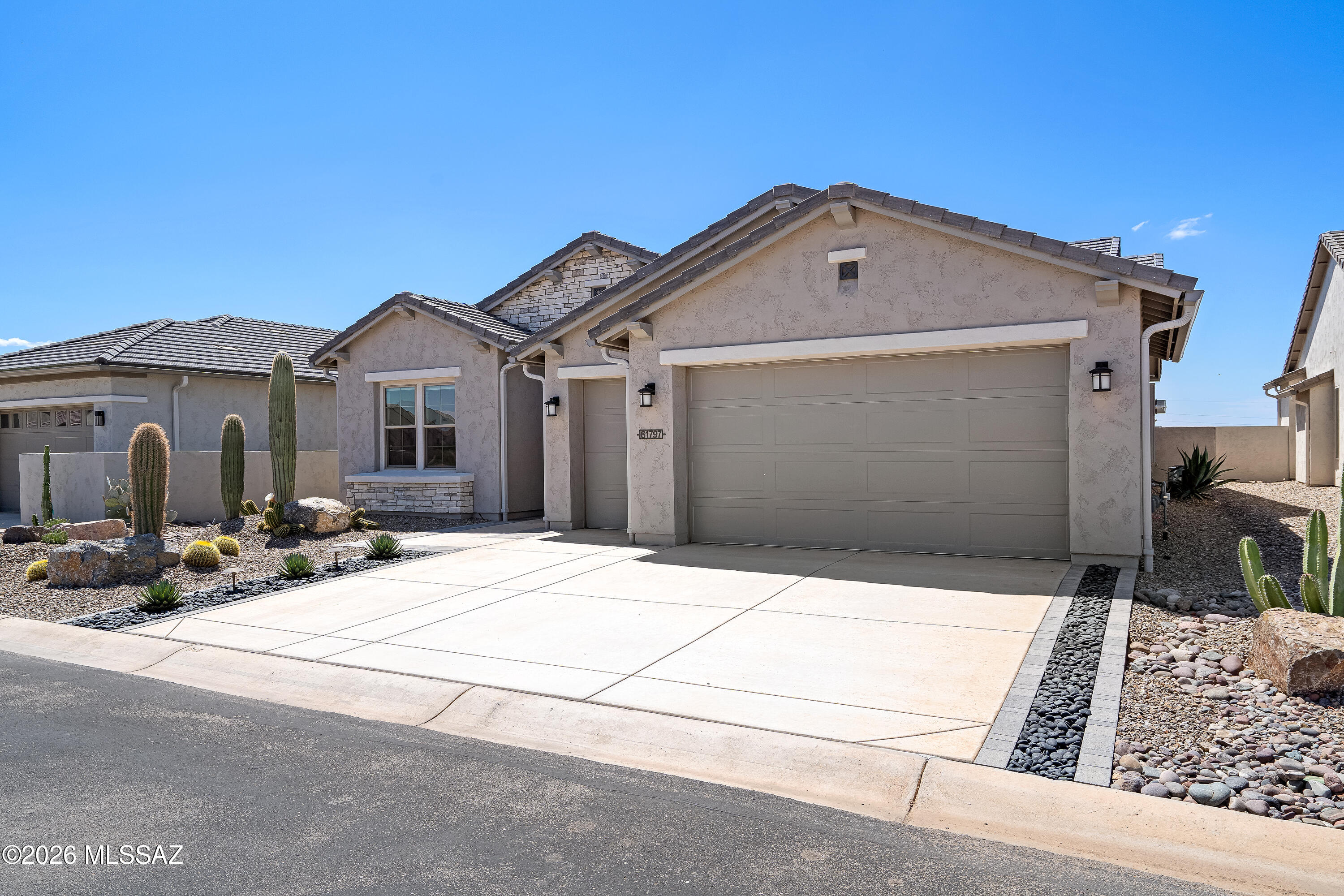 Stucco home with a two-car garage, wide driveway, and cactus landscaping.