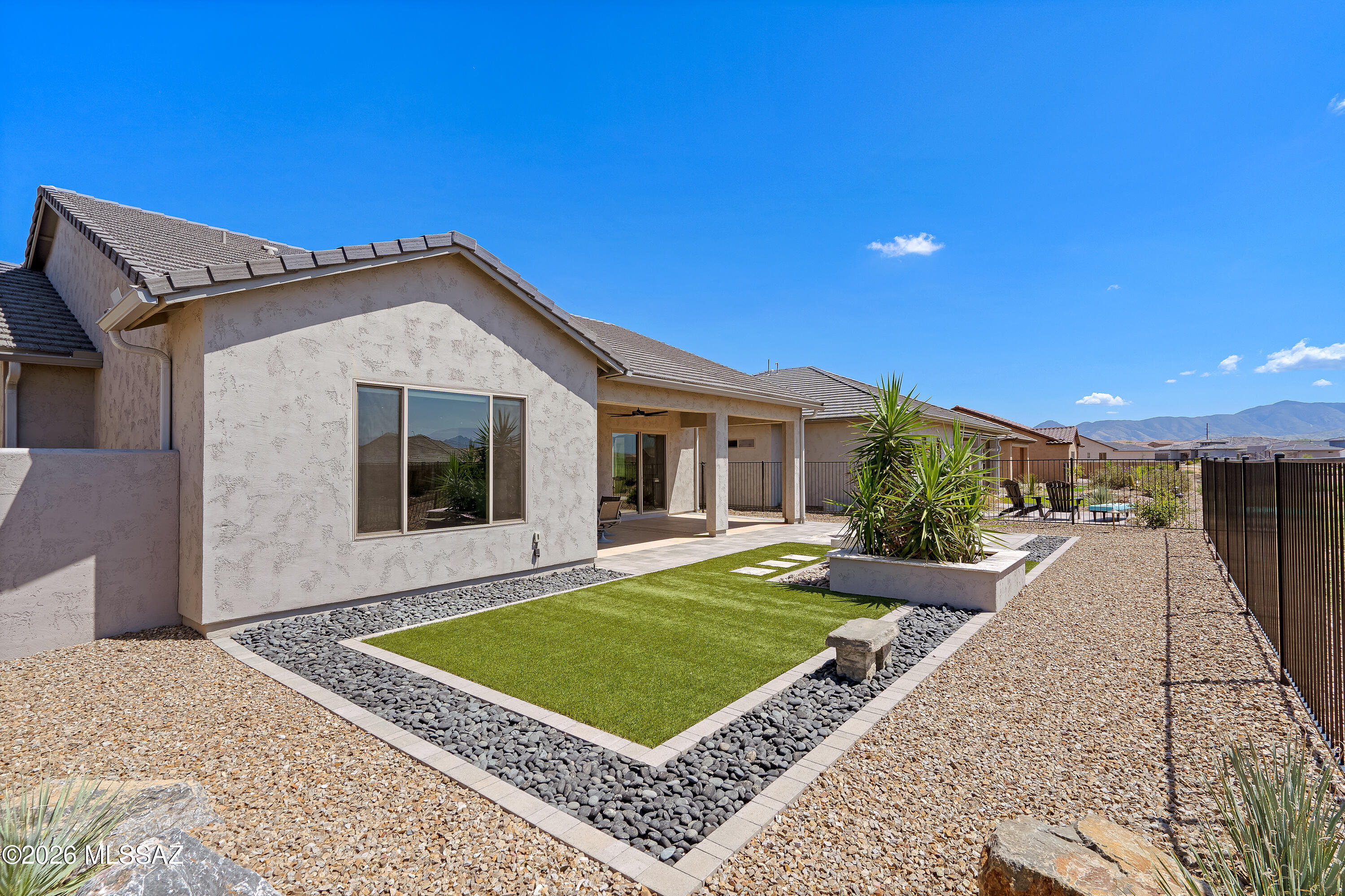 Backyard with a covered patio, geometric turf lawn, gravel landscaping, and mountain views.