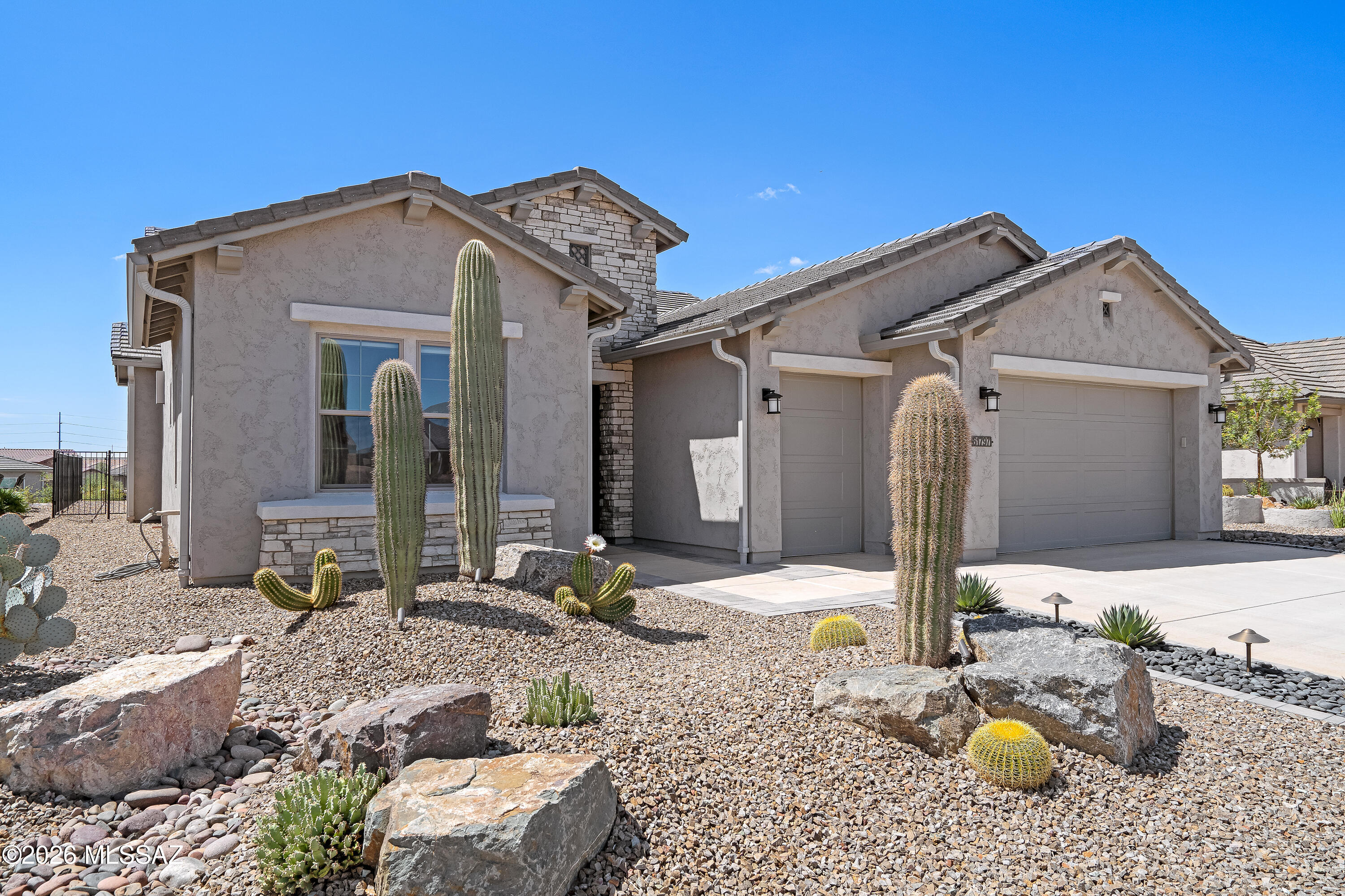 Stucco home with stone accents, a two-car garage, and cactus-filled desert landscaping.