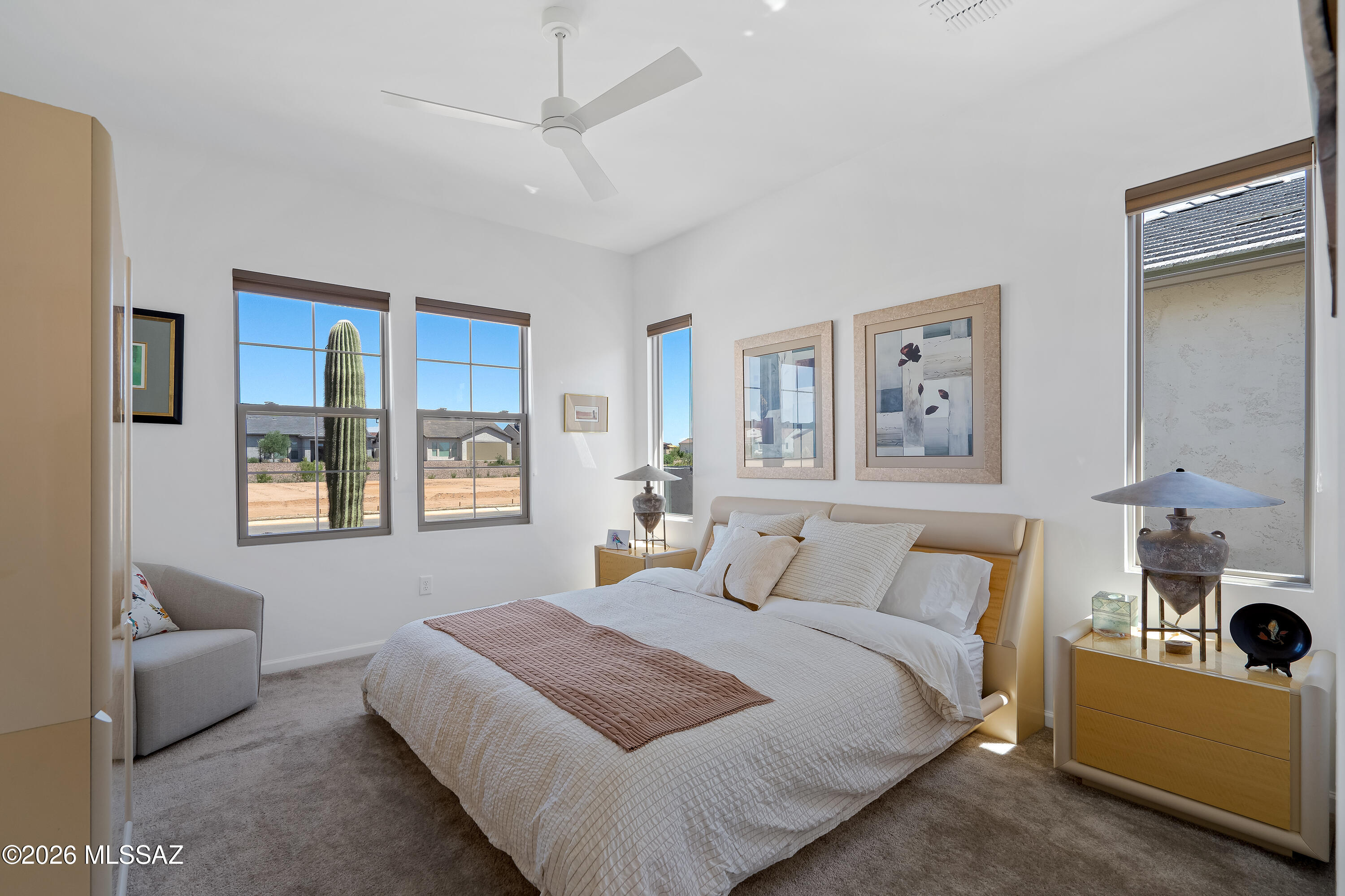 Furnished bedroom with a large bed and windows overlooking a tall cactus and desert neighborhood.