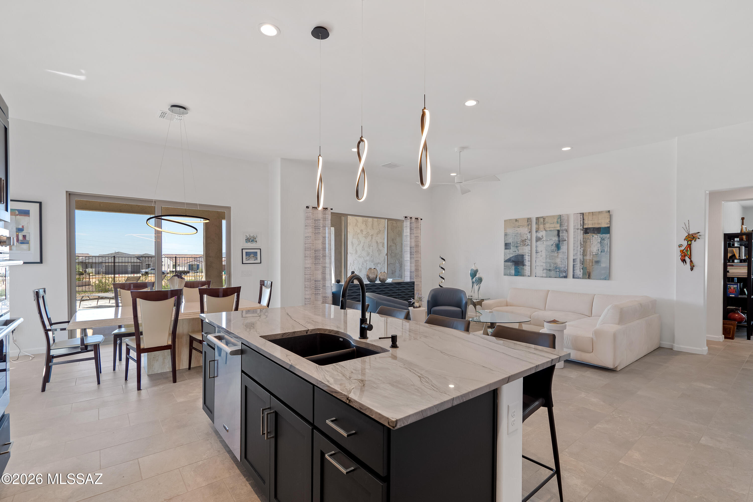 Open-plan kitchen with a large stone island, dining area, and white sectional by patio doors.