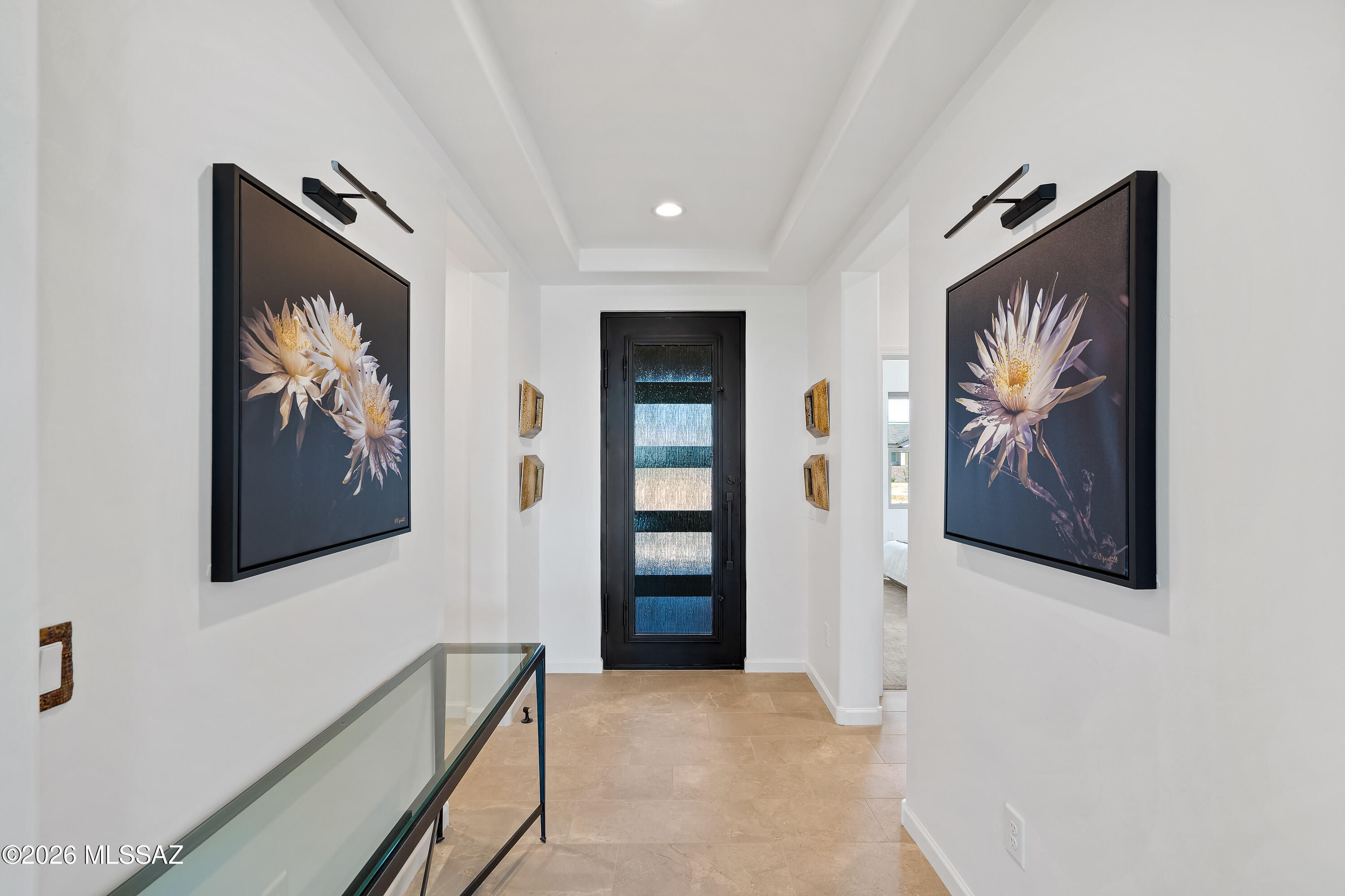 Entry hallway with a black glass-paneled front door, beige tile, floral art, and a glass console table.