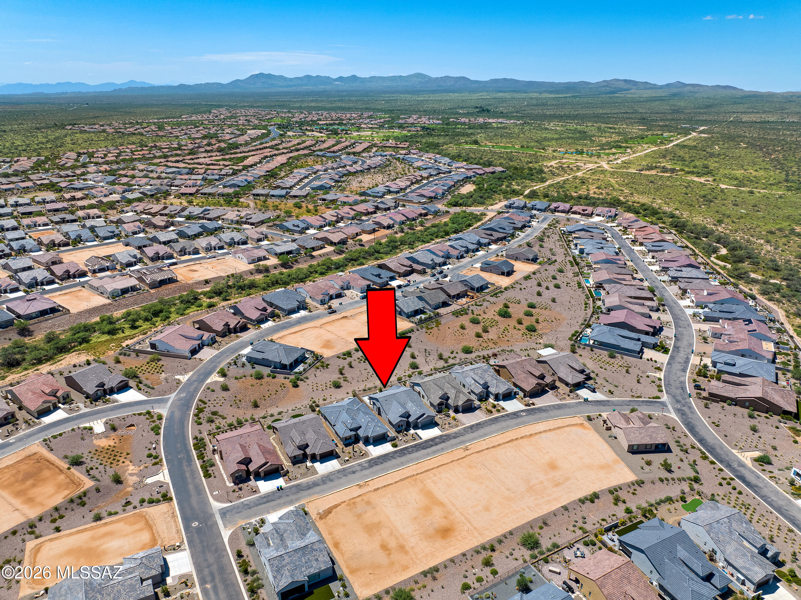 Aerial view of the home marked by a red arrow, surrounded by desert-subdivision homes and distant mountains.