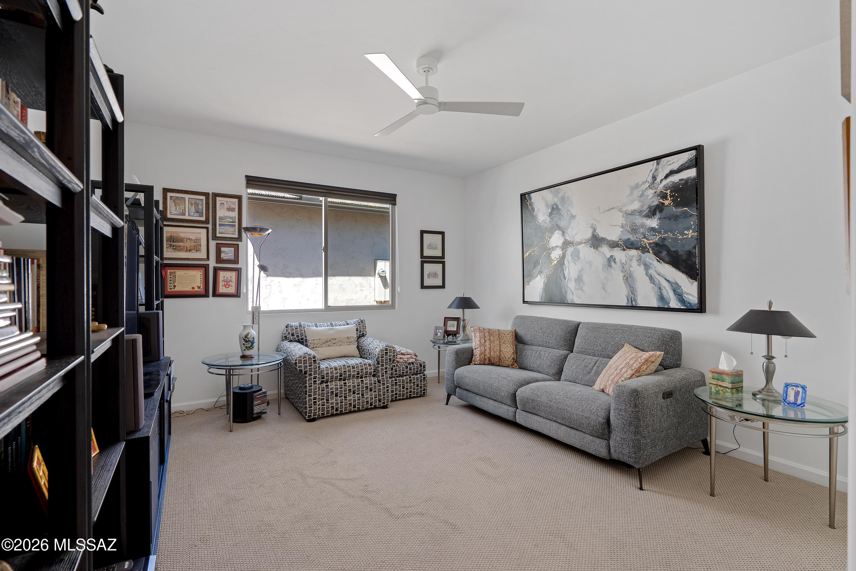 Living room with a gray sofa, patterned armchair, glass tables, and large abstract wall art.