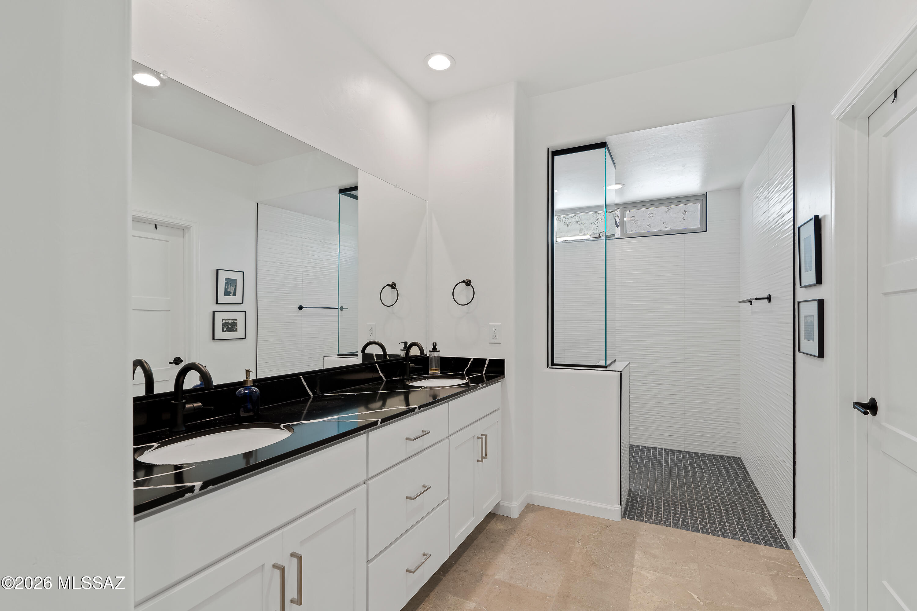 Modern bathroom with double vanity and black countertop beside a glass-enclosed tiled shower.