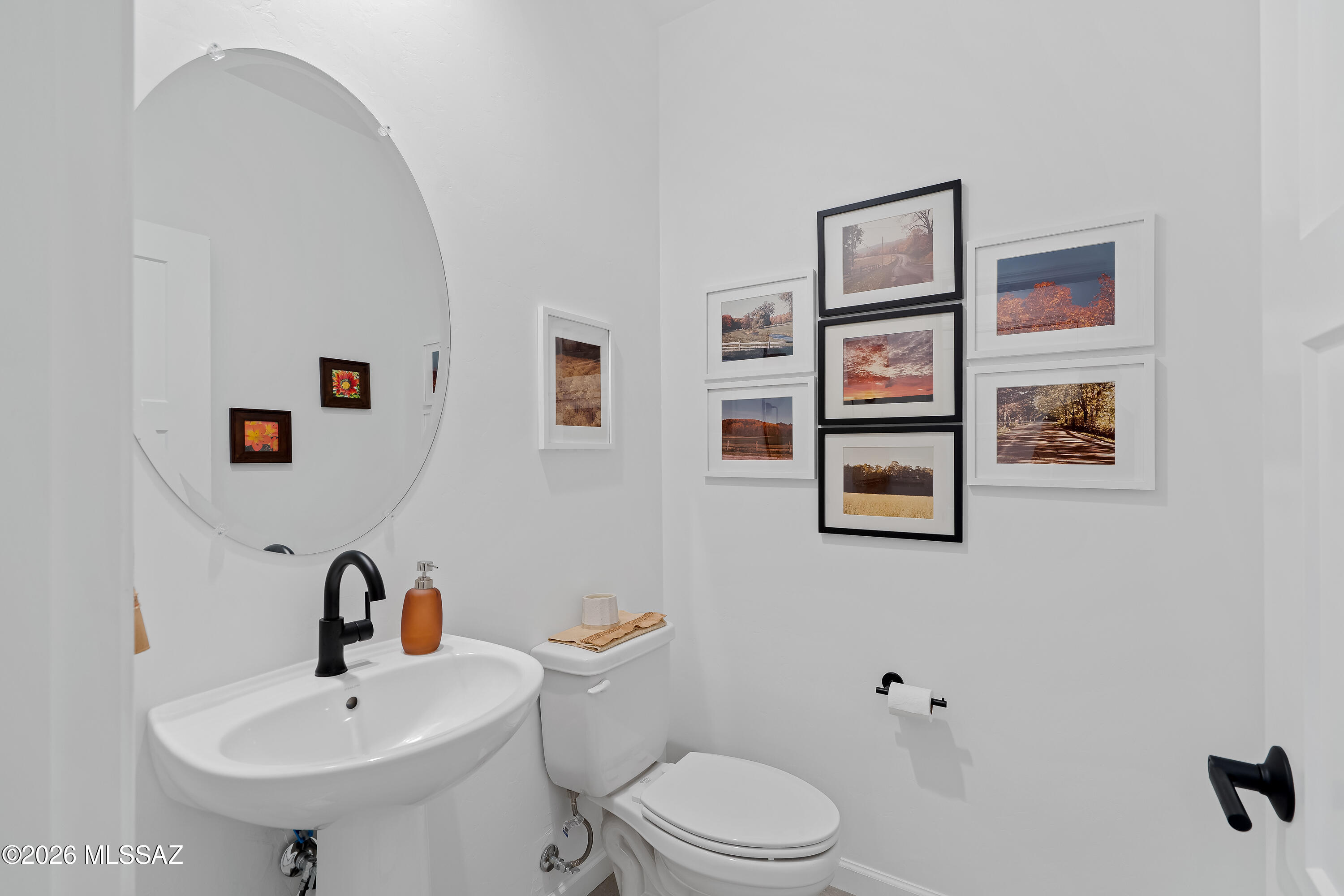 Bathroom with a wall-mounted sink, large round mirror, black fixtures, and framed landscape photographs.