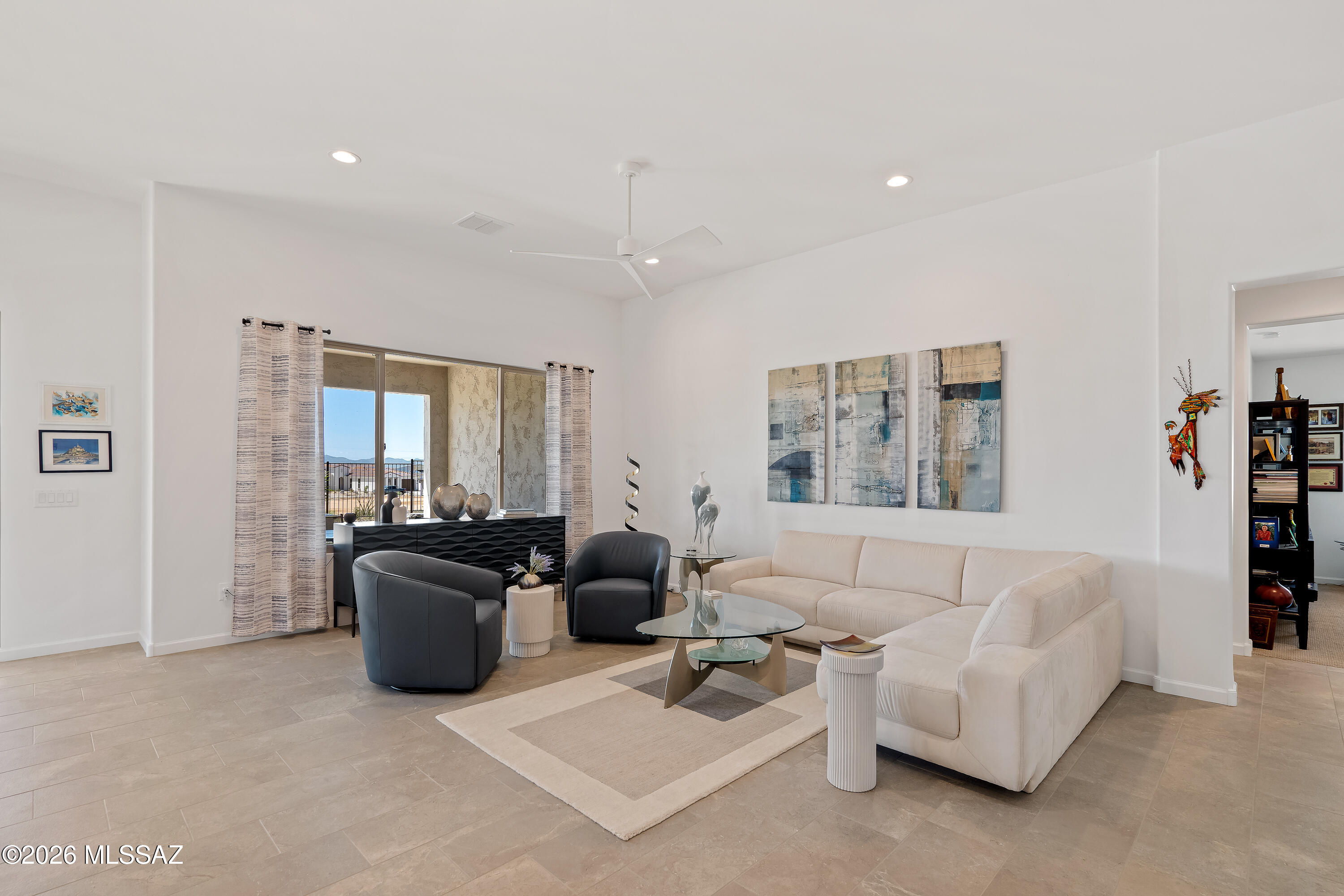 Furnished living room with a cream sectional, dark chairs, and sliding glass doors overlooking distant mountains.
