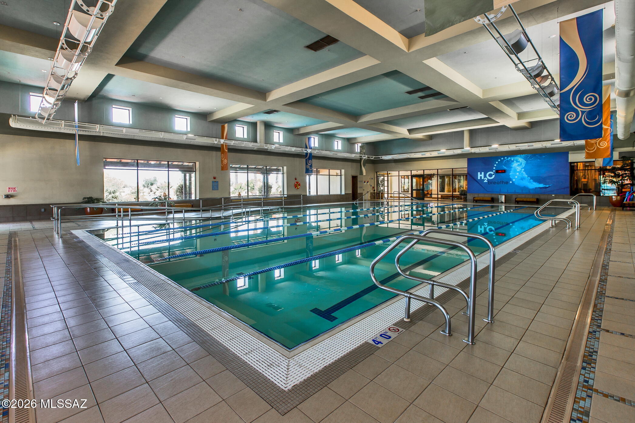 Indoor swimming pool with blue lane ropes, tiled deck, and metal entry rails.