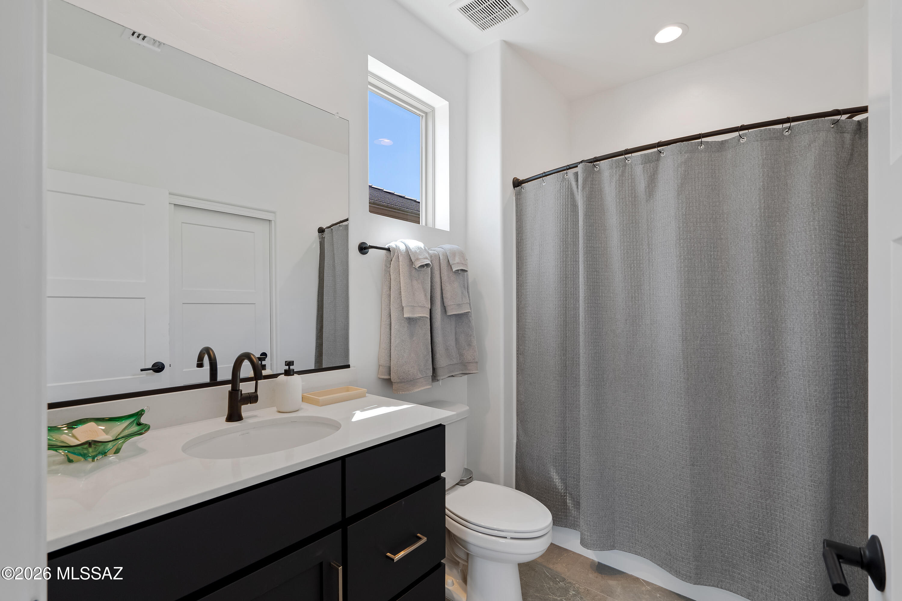 Bathroom with a black vanity, white sink, gray shower curtain, and high window.