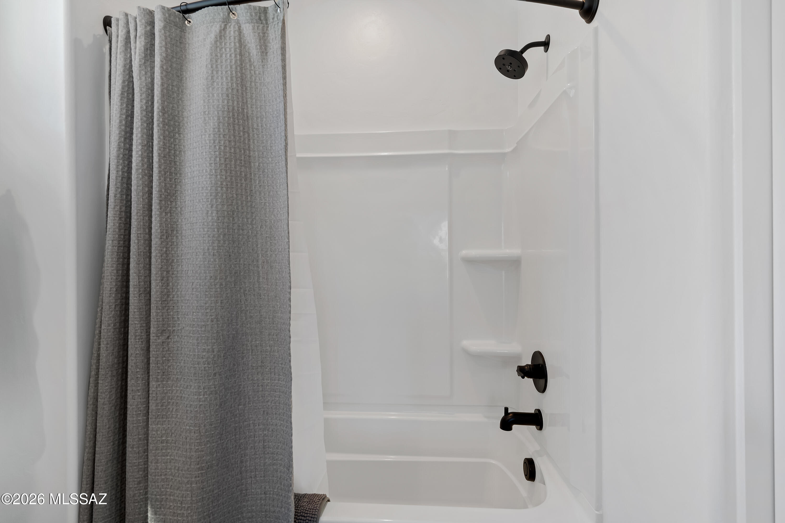 White bathtub and shower with a gray curtain and black fixtures.