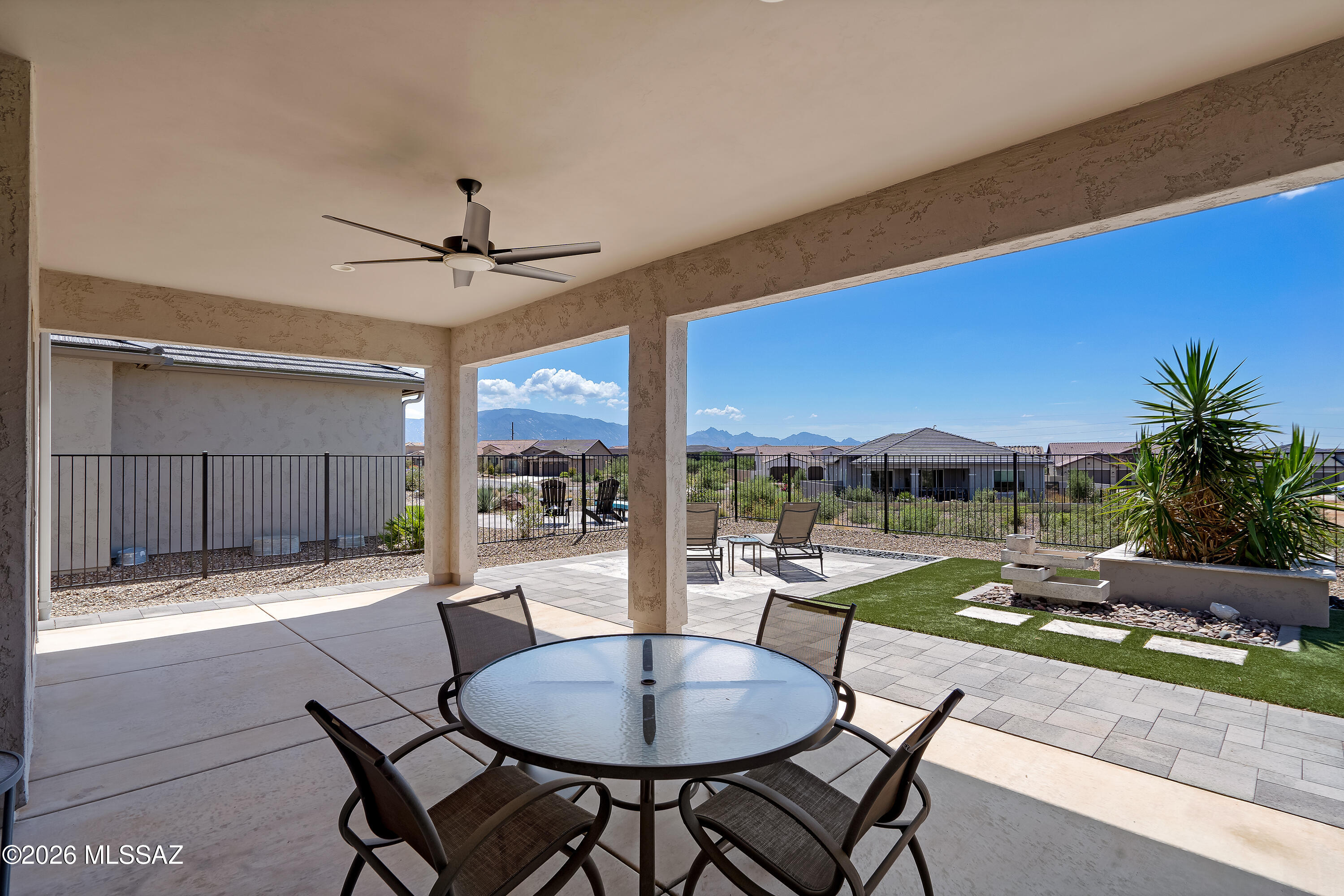 Covered patio with dining set, artificial turf, desert landscaping, and distant mountains.