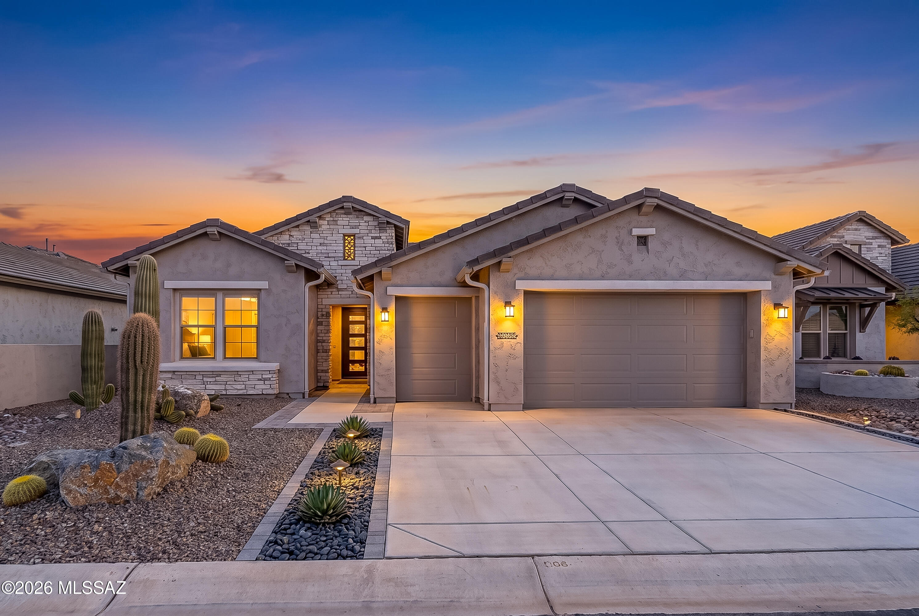 Stucco and stone home at dusk with a two-car garage and cactus landscaping.