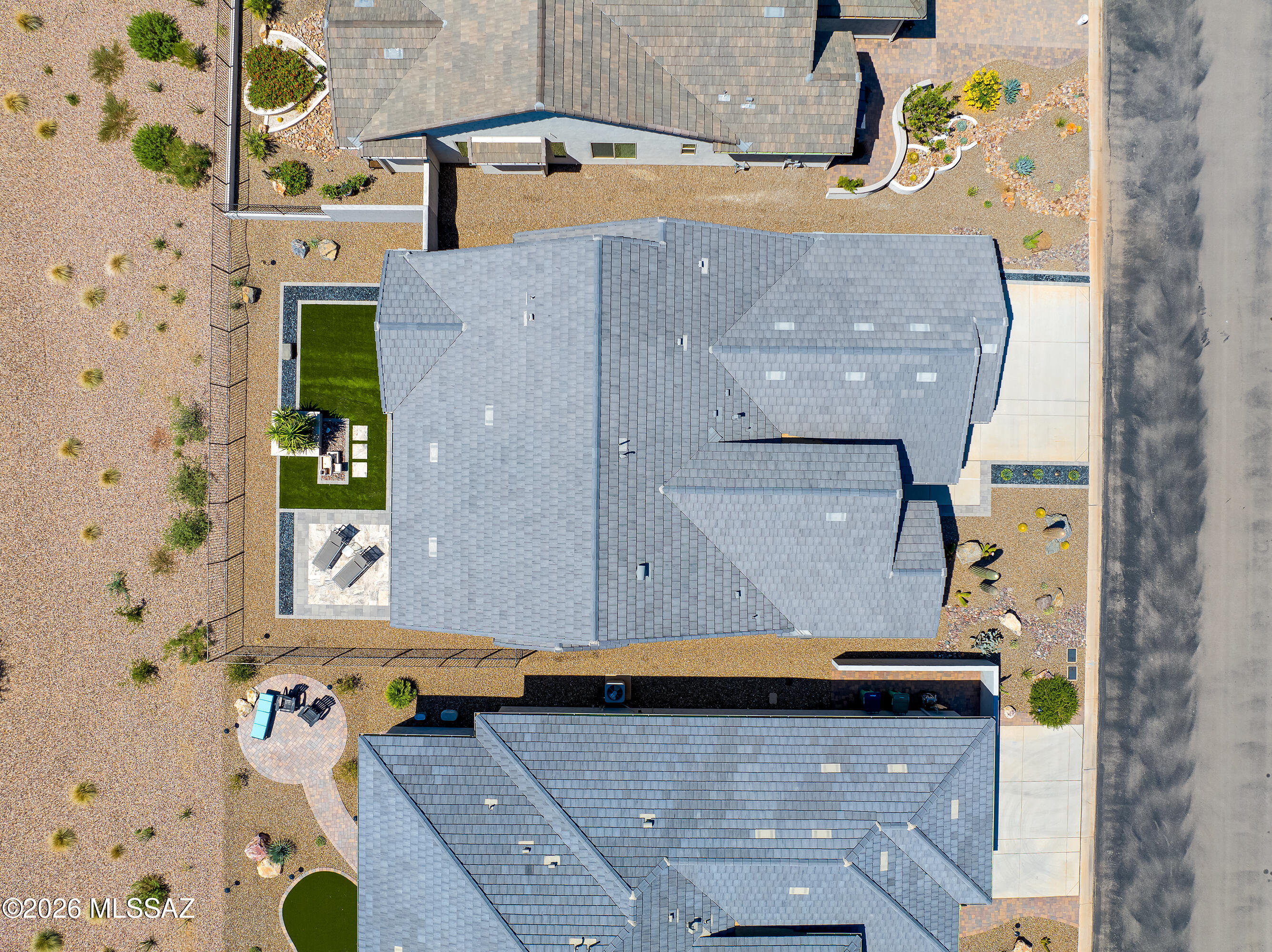 Aerial view of a home with gray tiled roofs, desert landscaping, and a fenced turf yard.