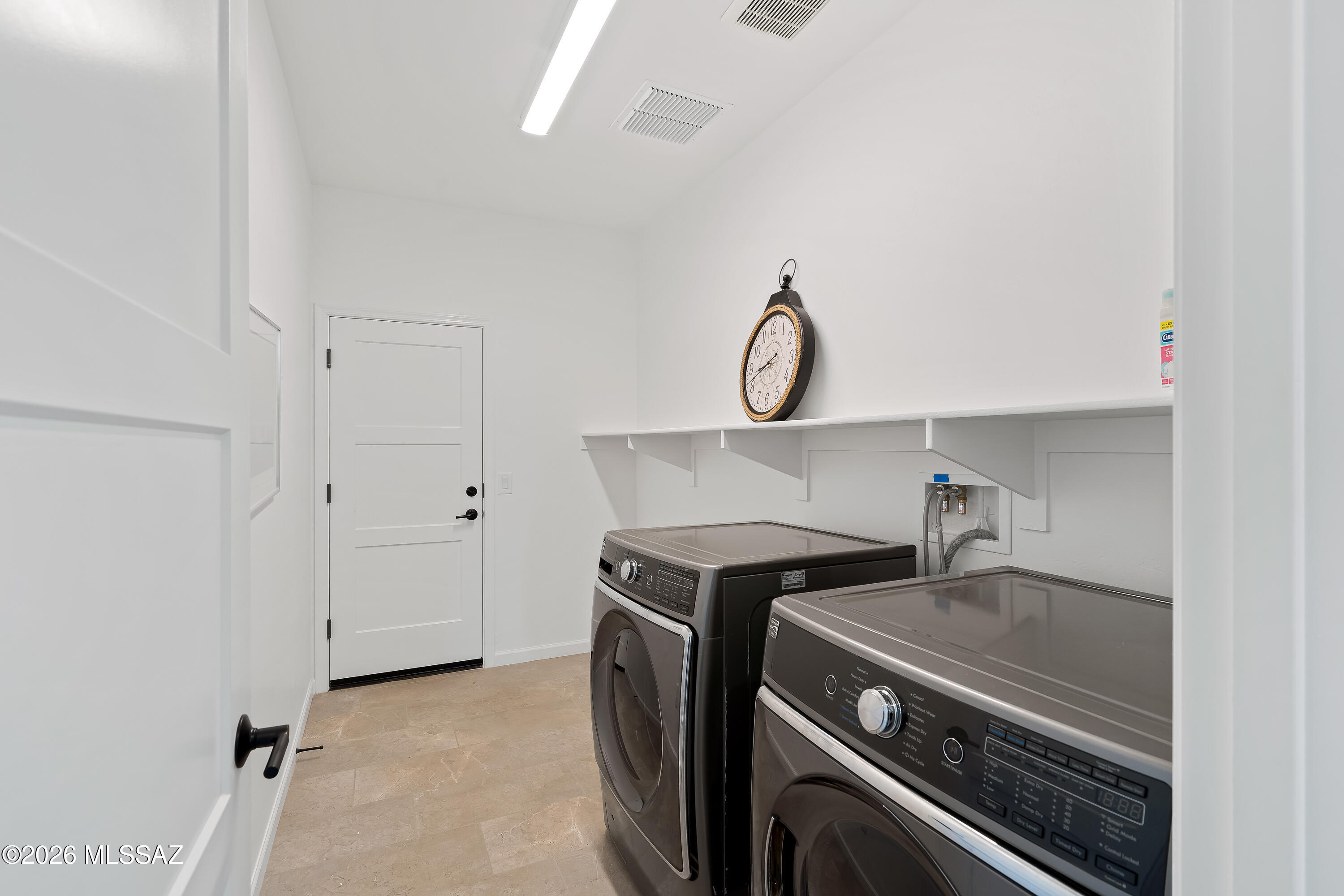 Laundry room with dark front-loading washer and dryer beneath a long wall shelf.