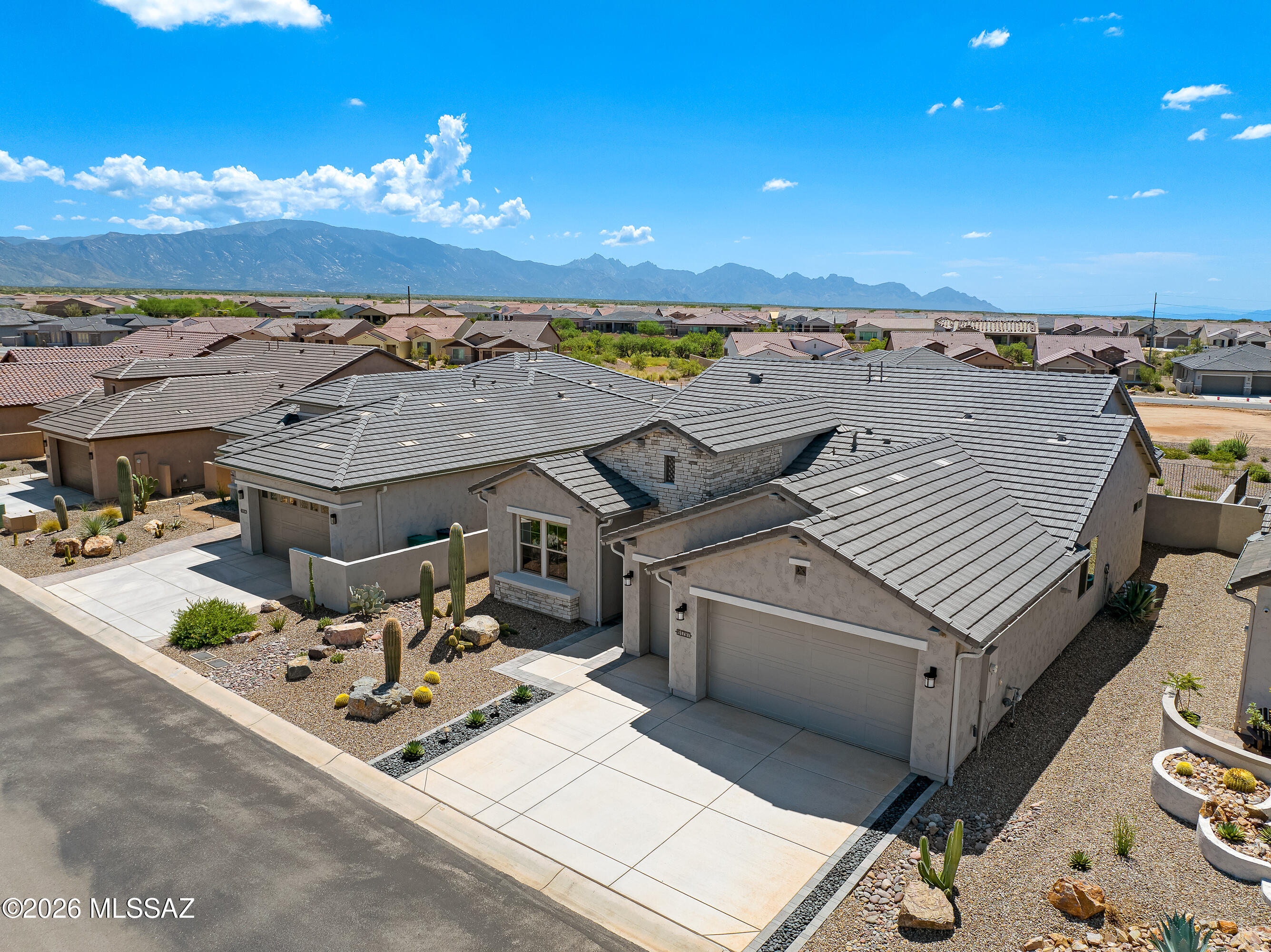 Aerial view of a stucco home with gray tile roofs, desert landscaping, and mountains beyond.