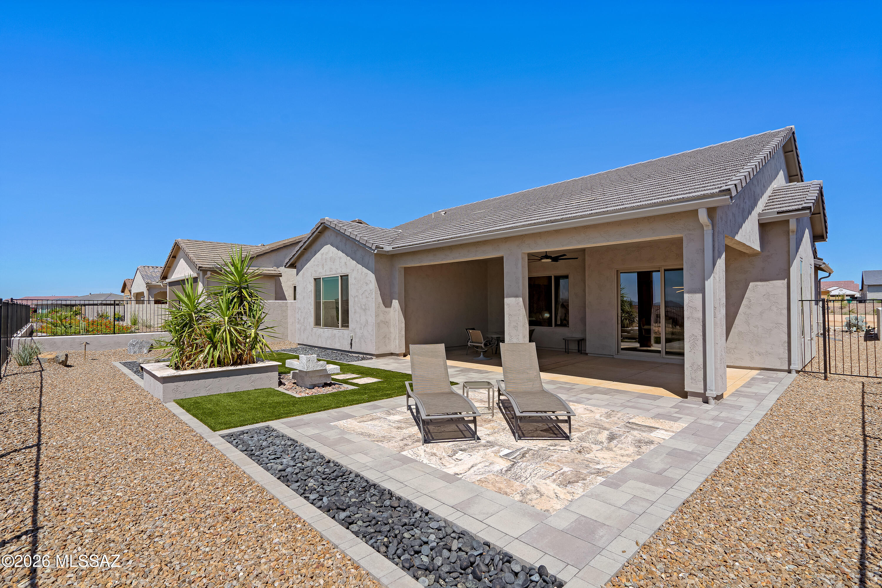 Home’s rear patio with covered seating, lounge chairs, paved terrace, and desert landscaping.