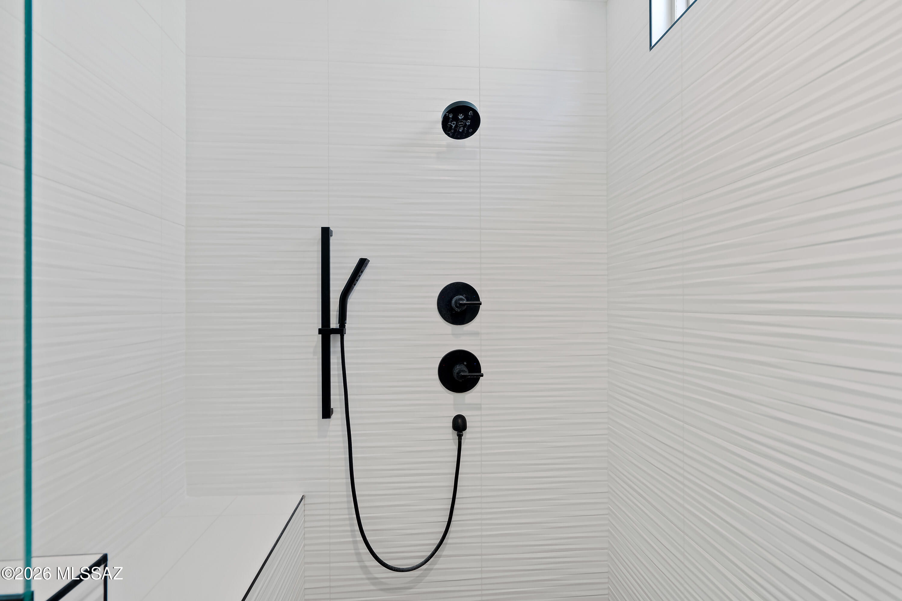 Walk-in shower with matte black fixtures, white textured tile, and a glass enclosure.