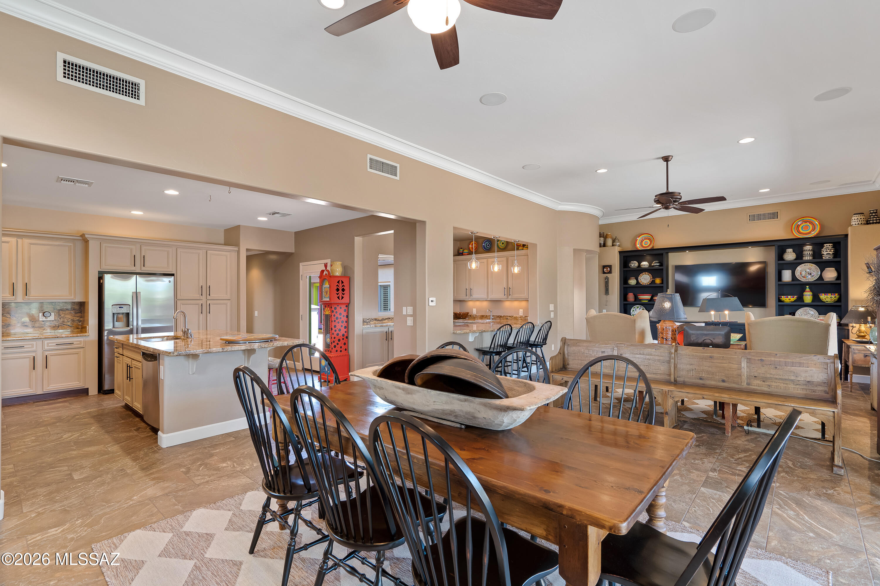Open-plan kitchen and dining room with a large wood table, stone island, and built-in media wall.