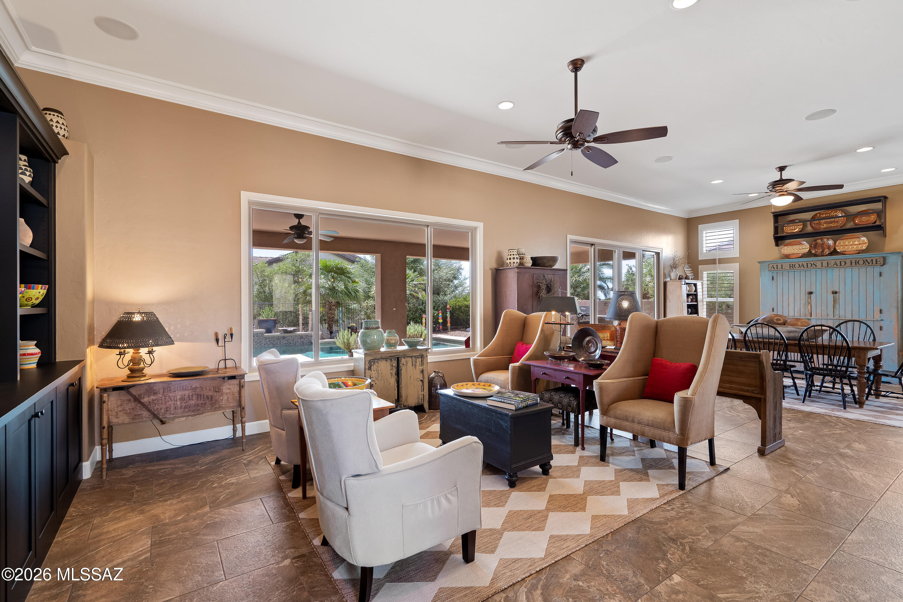Furnished living room with large windows overlooking a pool and greenery, adjoining a dining area.