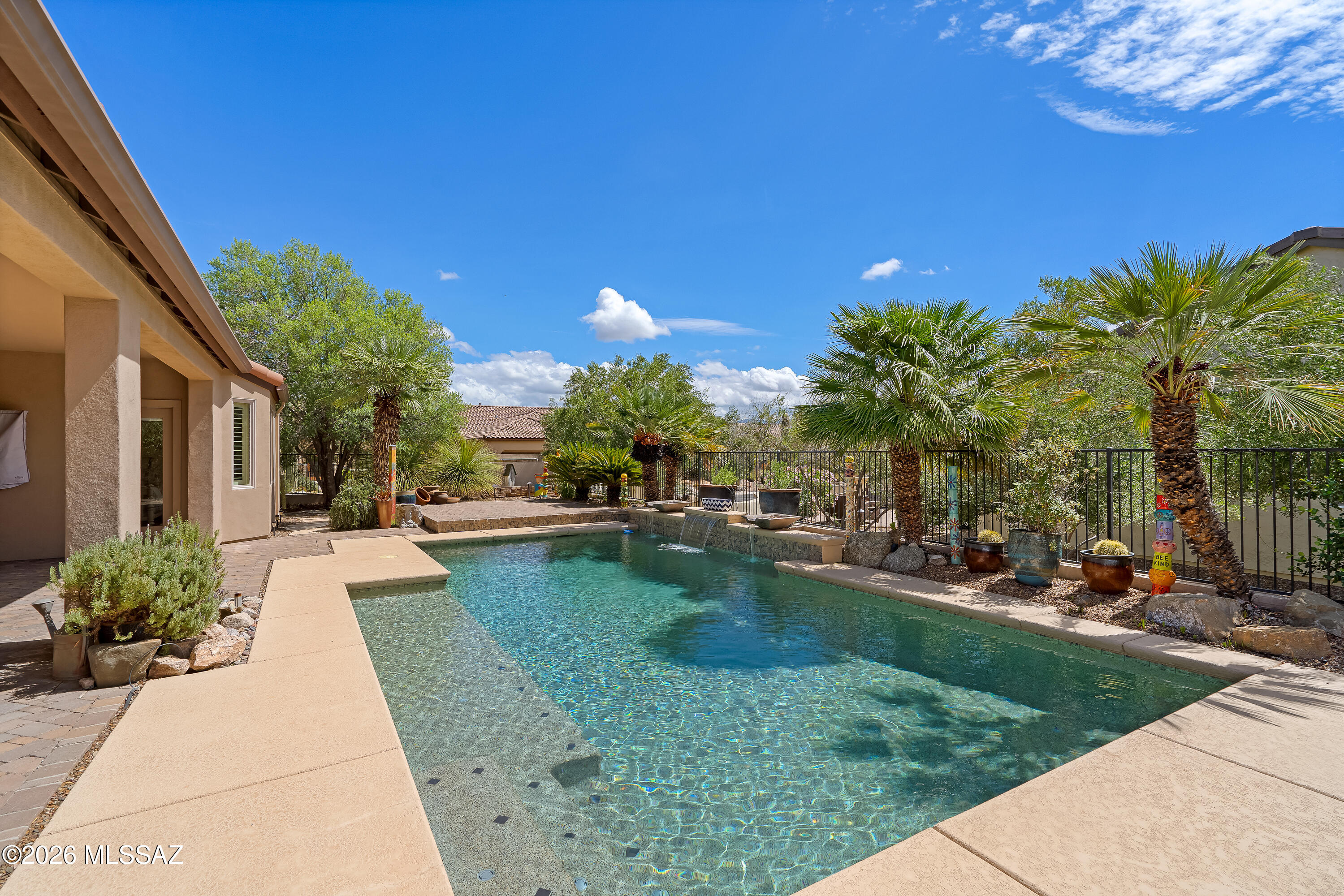 Backyard swimming pool with a waterfall, palm trees, and a covered patio.