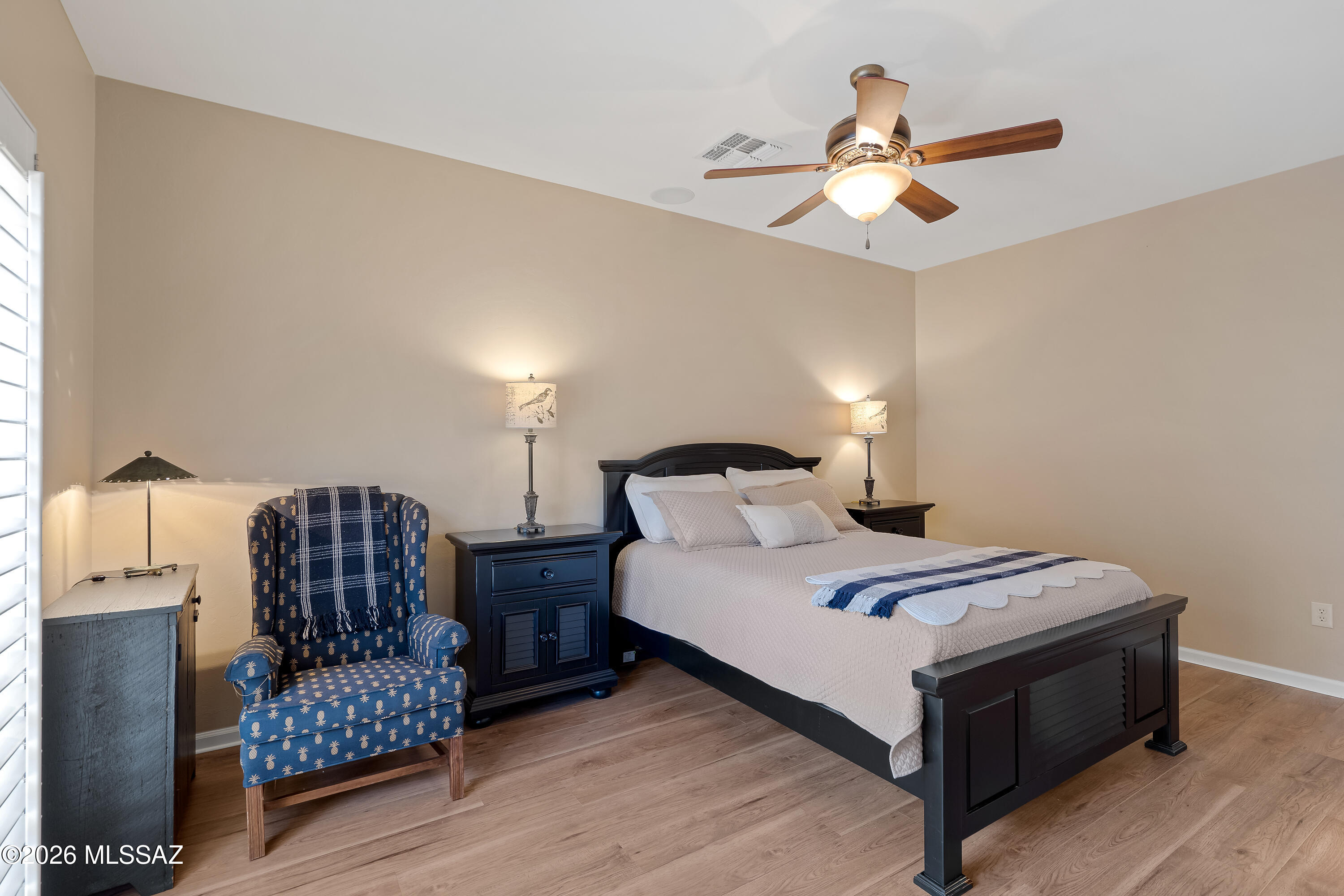 Bedroom with a dark wood bed, navy throw, blue patterned armchair, and ceiling fan.