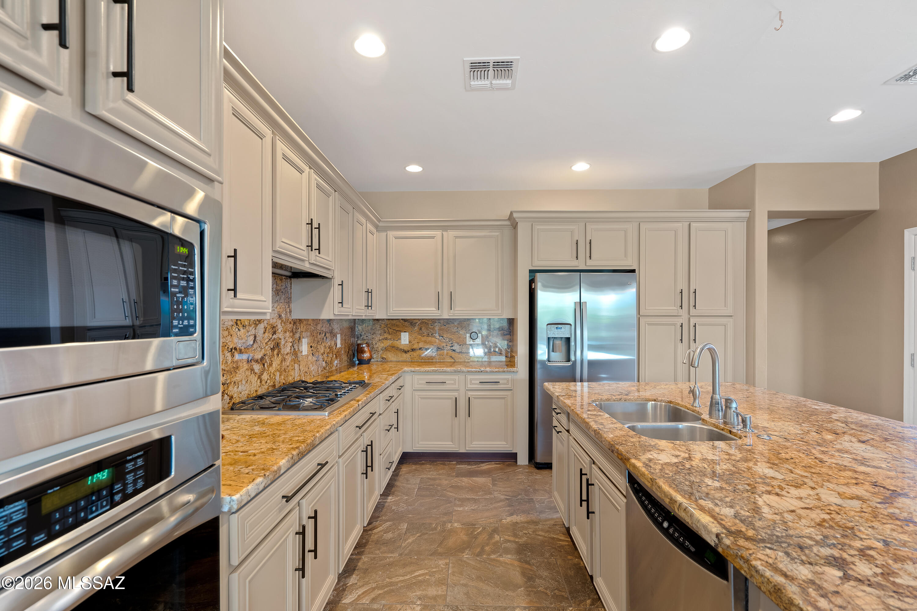 Kitchen with granite counters, cream cabinets, stainless appliances, and a large sink island.