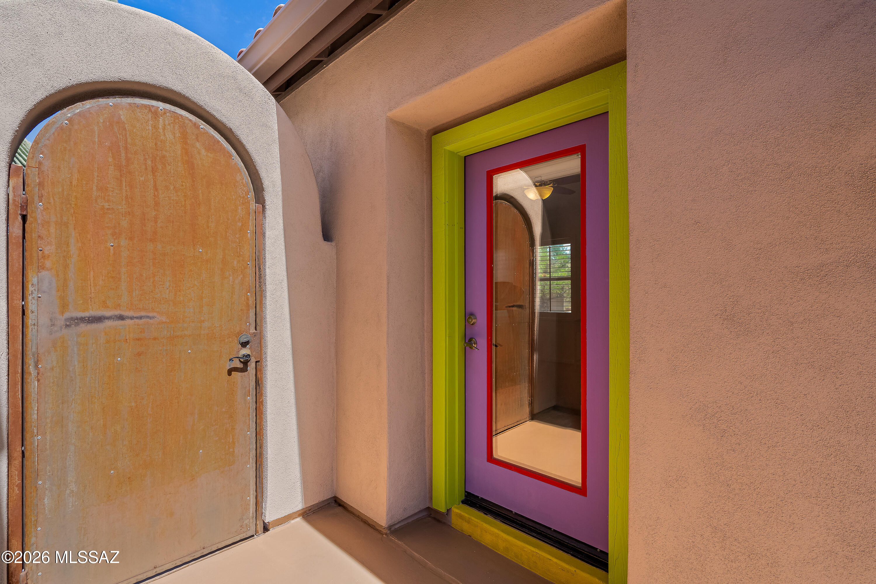 Southwestern home entry with an arched metal door and a purple glass-panel door in lime-green trim.