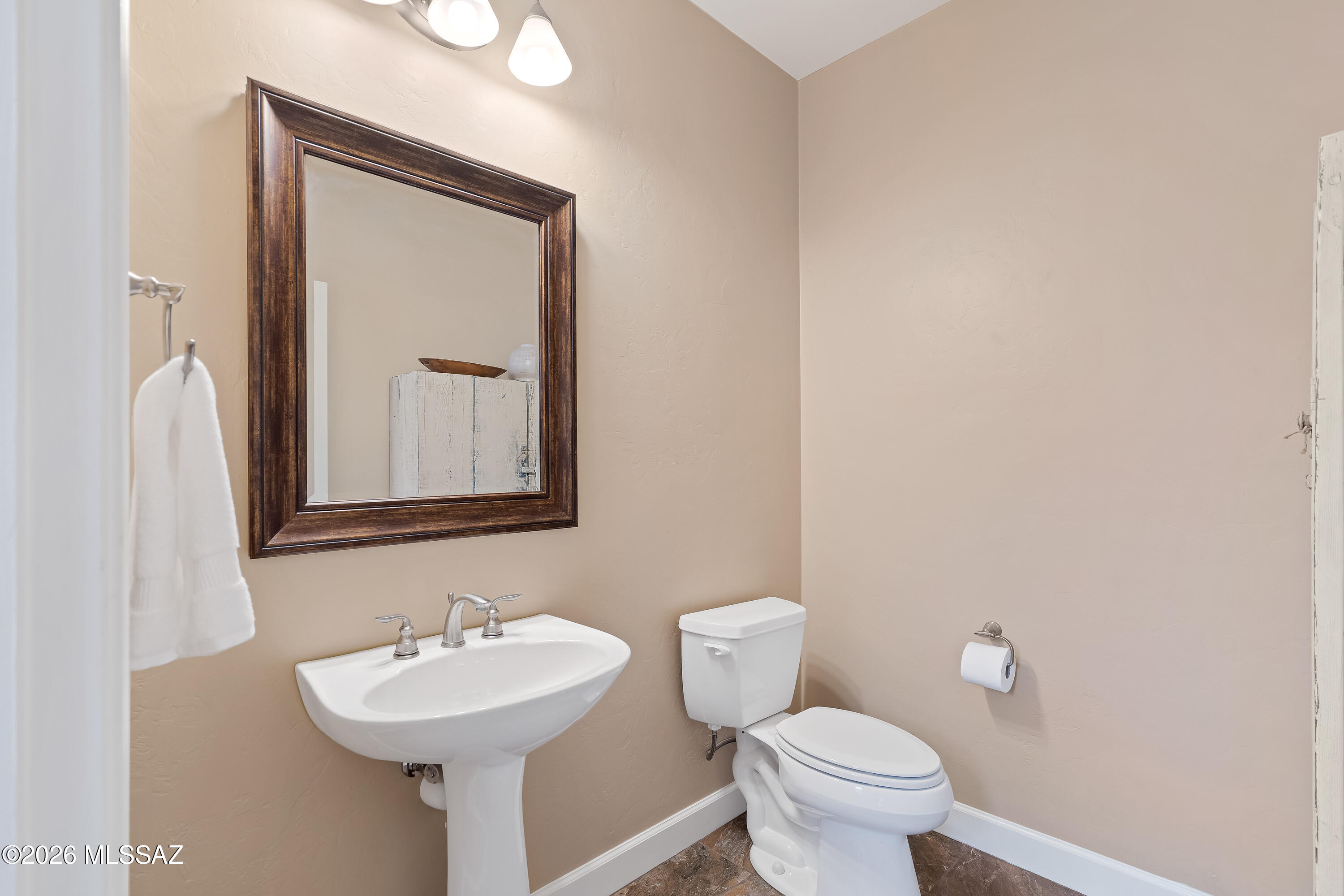 Bathroom with a pedestal sink, toilet, and large dark wood-framed mirror.