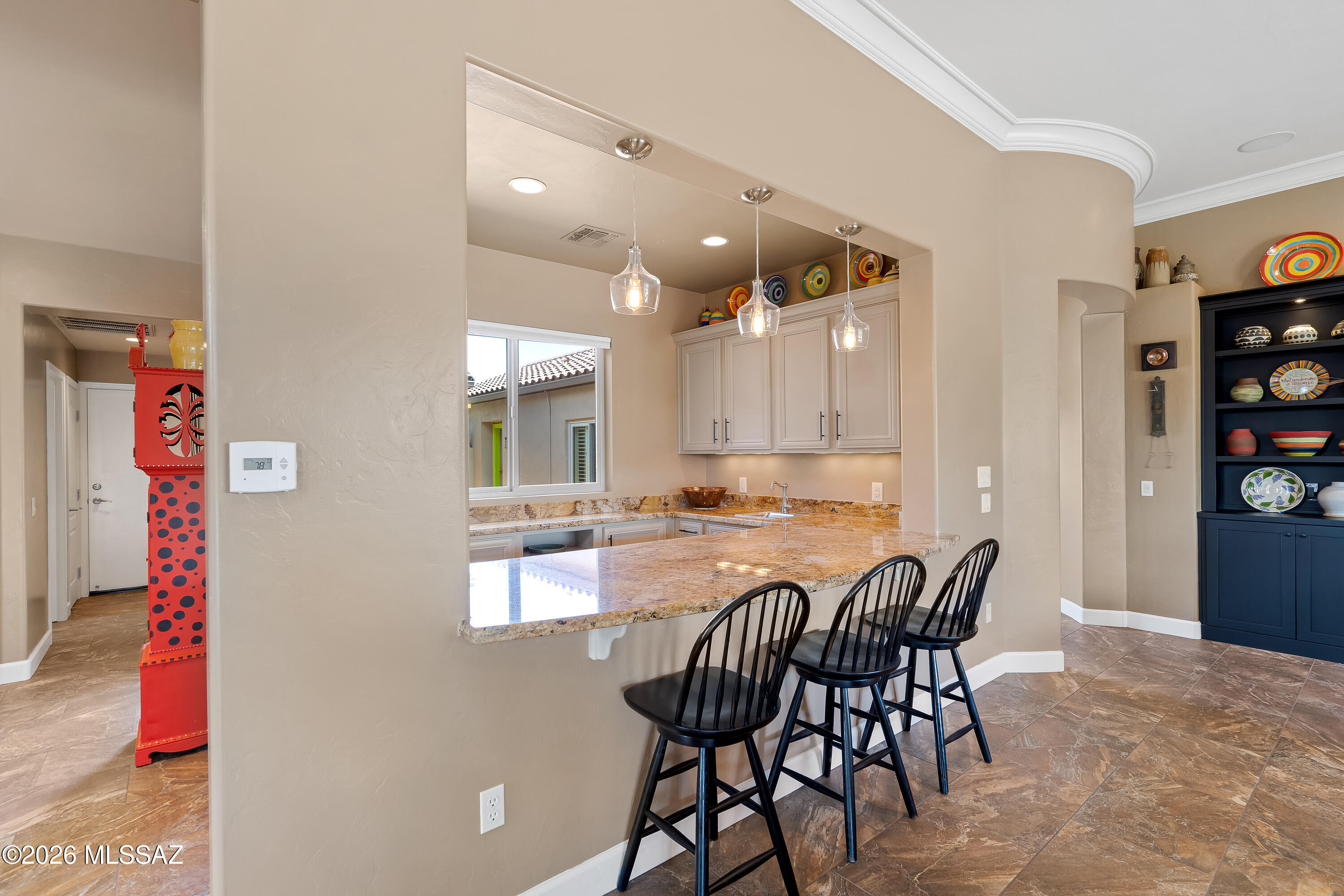 Kitchen with a granite breakfast bar, black stools, pendant lights, and colorful pottery.