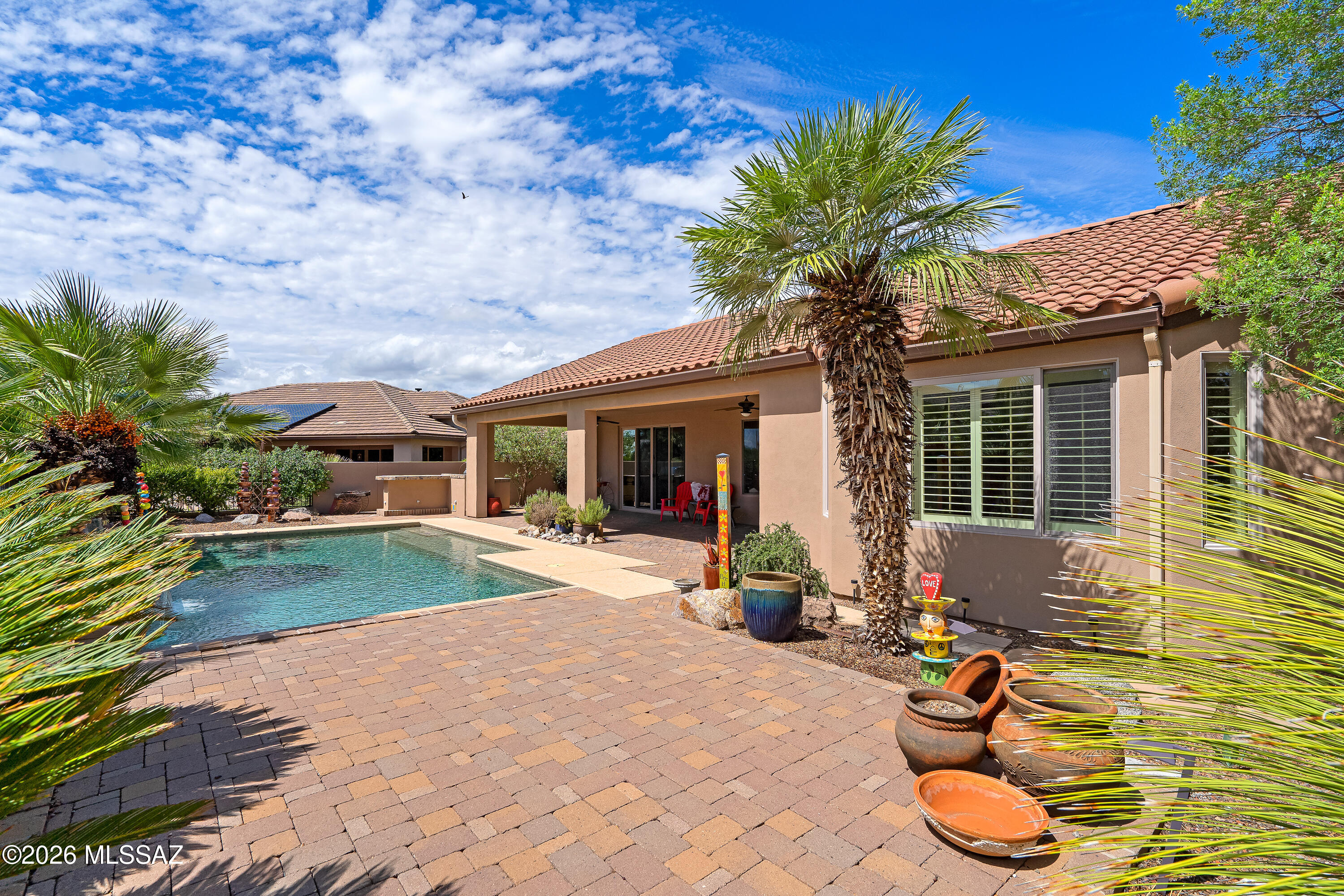 Stucco home with a backyard pool, covered patio, paver deck, and palm trees.