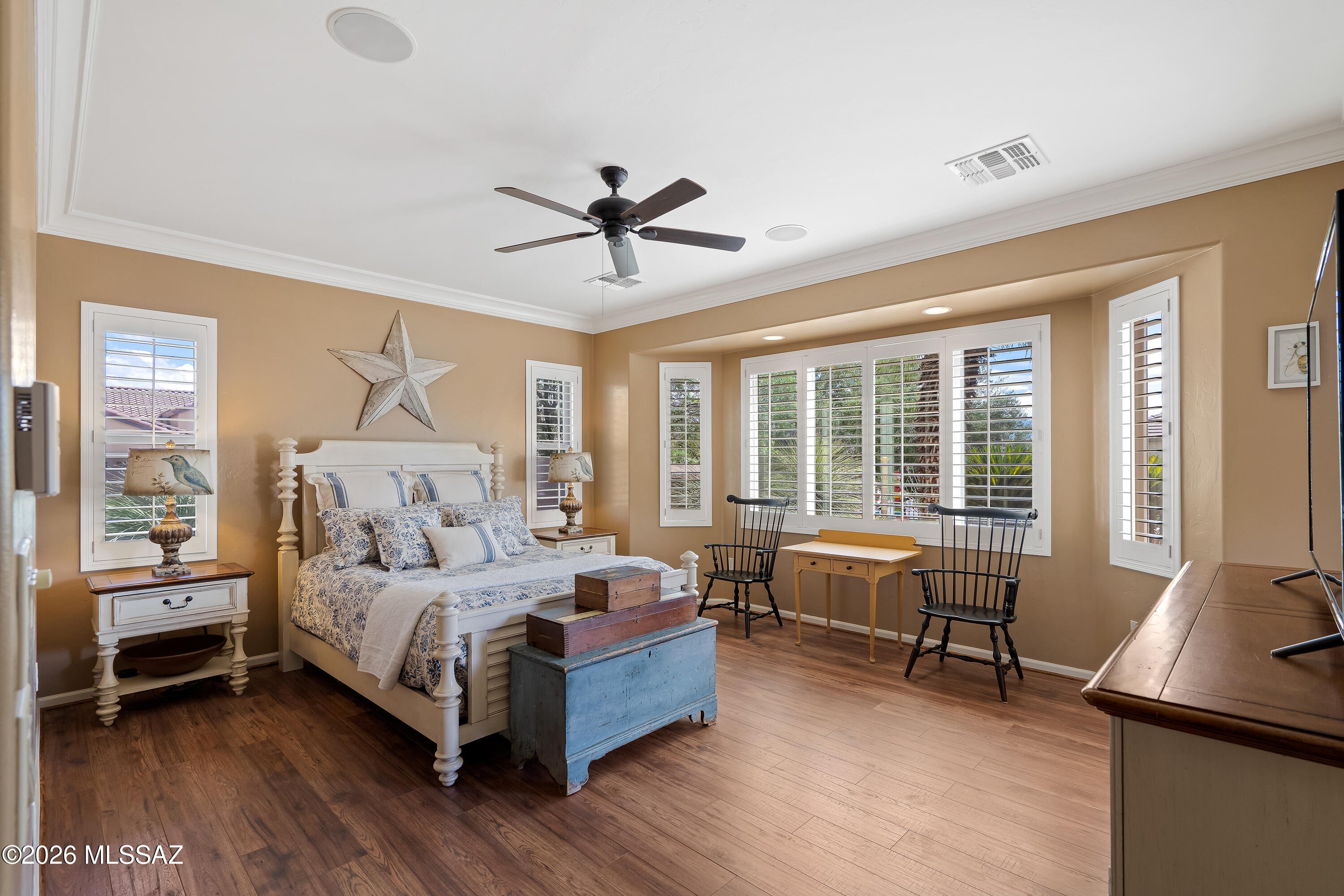 Bedroom with blue-and-white bedding, plantation shutters, and a small desk by the windows.