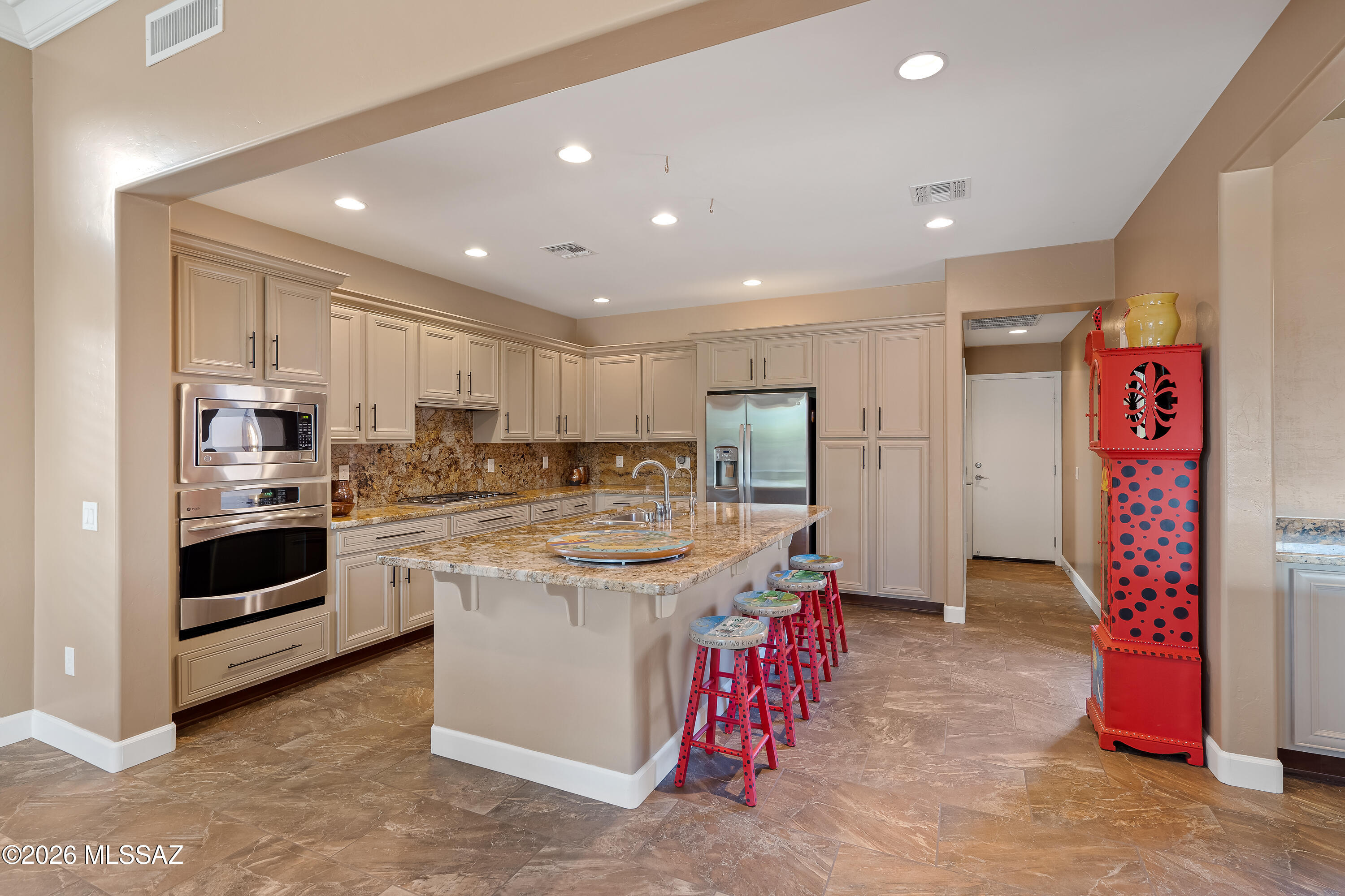 Kitchen with a granite island, stainless steel appliances, and bright red bar stools.