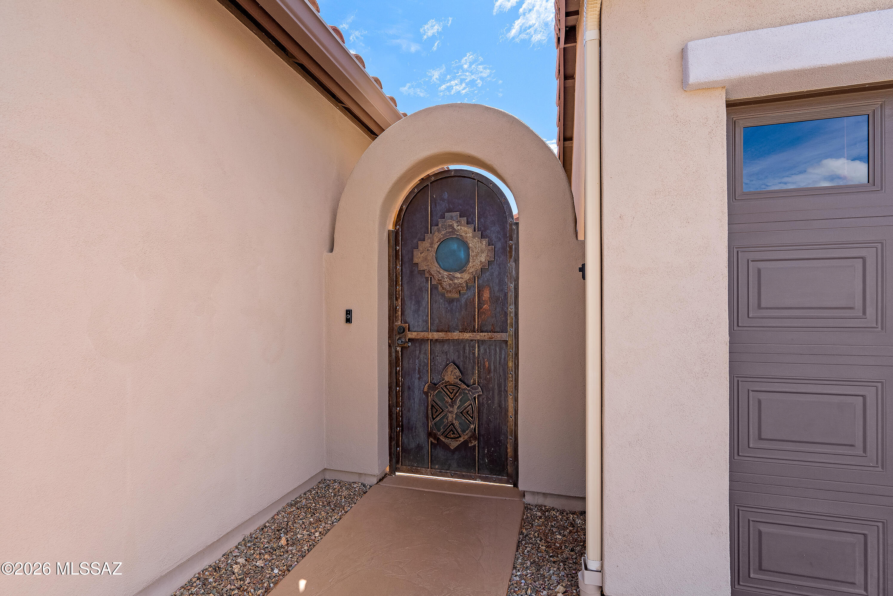 Stucco home entry with an arched wooden door, blue glass inset, and decorative metalwork.