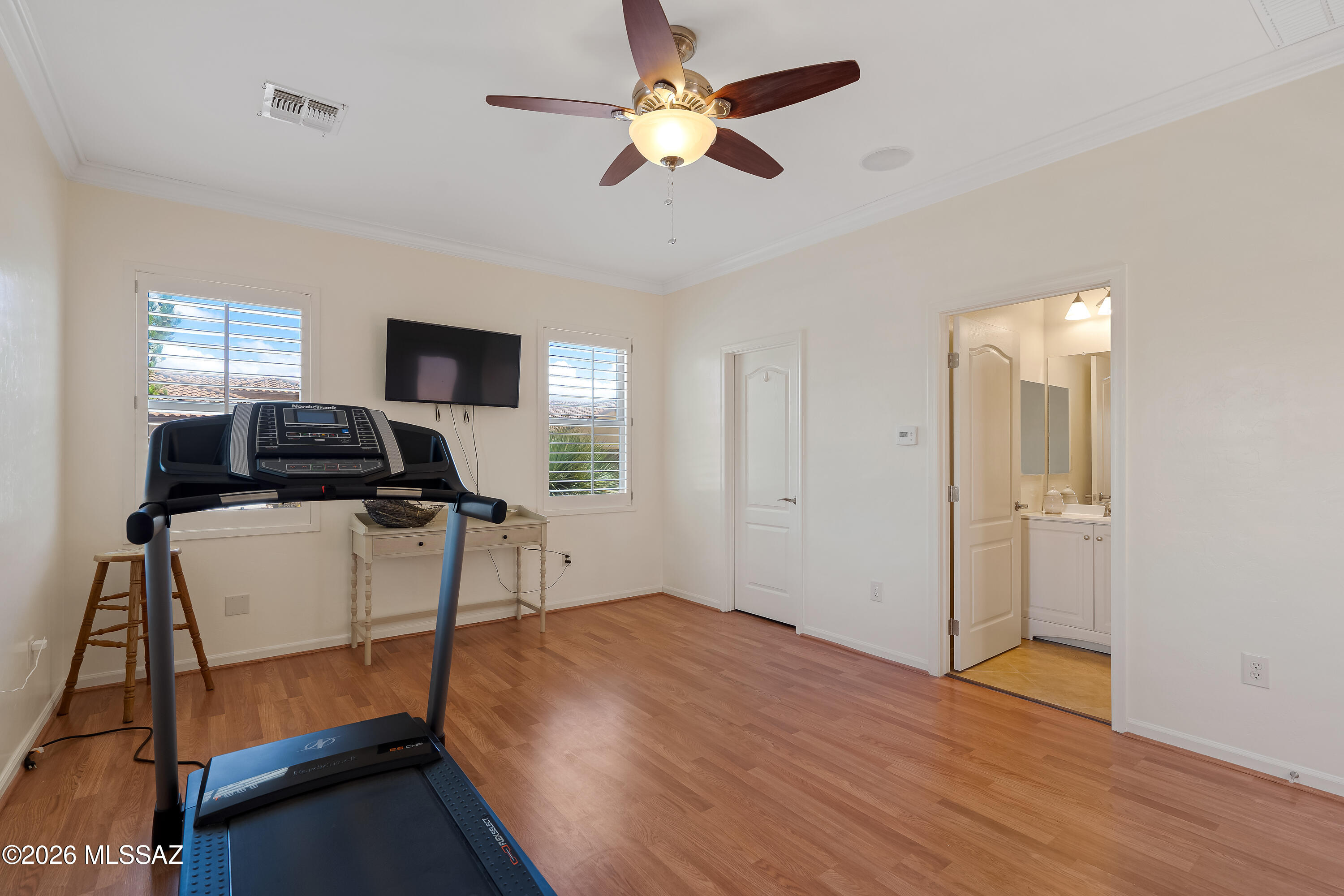 Home exercise room with a treadmill, hardwood floors, and shuttered windows.
