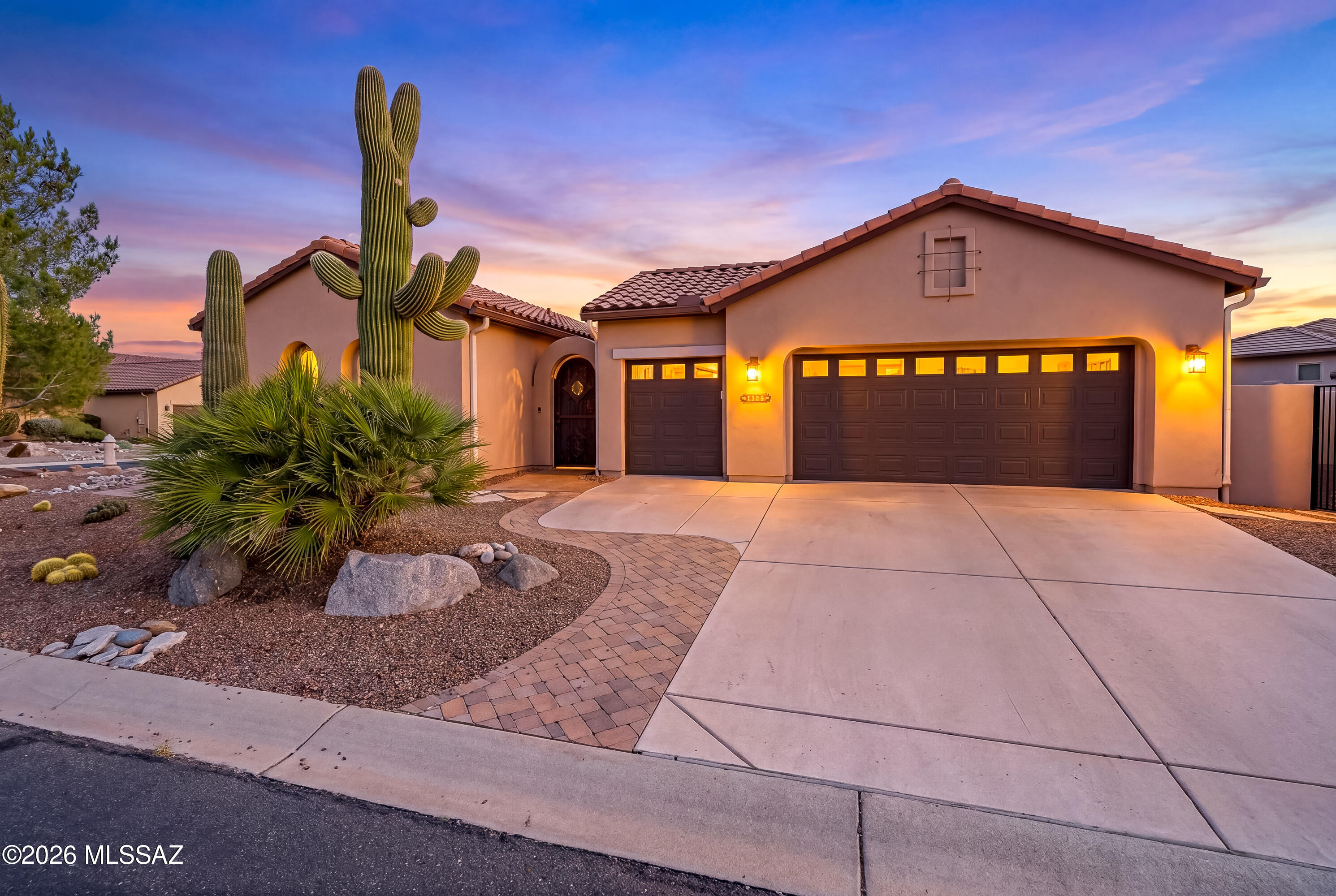 Southwestern-style home with a double garage, framed by saguaro cacti at dusk.