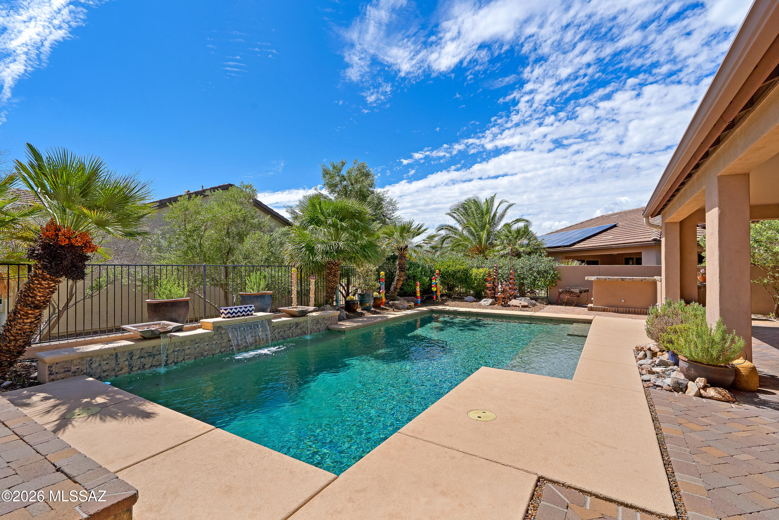 Backyard swimming pool with a raised waterfall feature, palm trees, and covered patio.